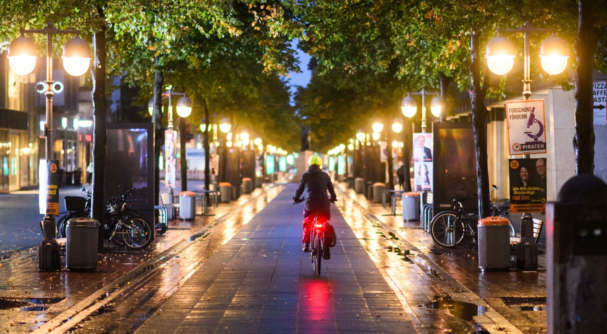 Eine Radfahrerin fährt am frühen Morgen zwischen Straßenlaternen durch die Innenstadt von Hannover.