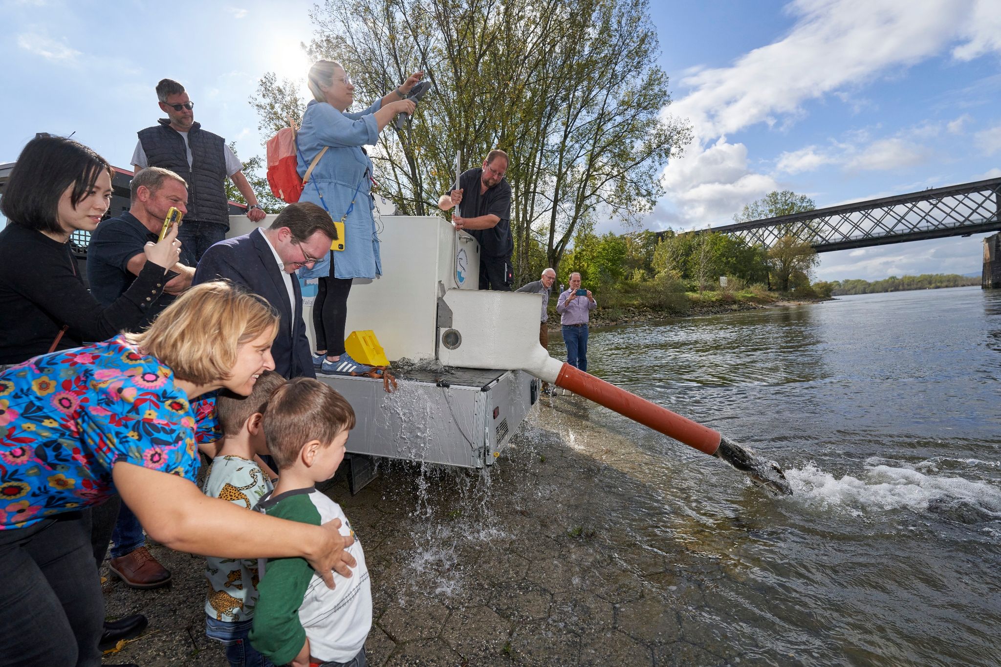 Die rheinland-pfälzische Klimaschutzministerin Katrin Eder (l) steht mit ihren beiden Söhnen am Rhein und beobachtete das Freilassen der rund 400 Aale.
