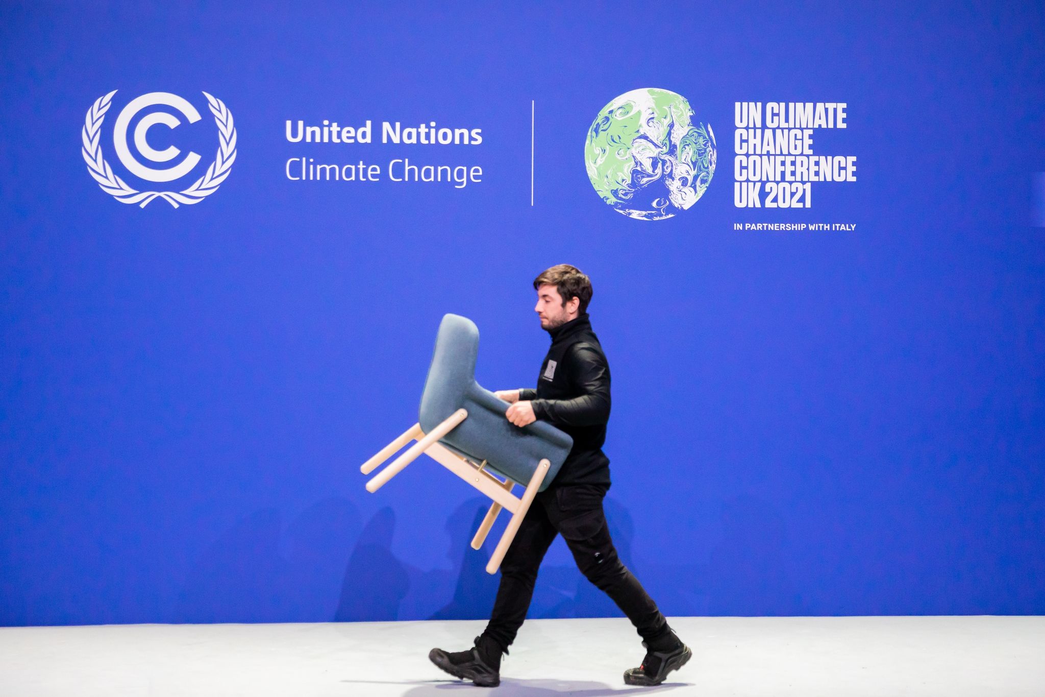 Ein Mitarbeiter trägt bei der UN-Klimakonferenz COP26 einen Stuhl von einer Bühne.