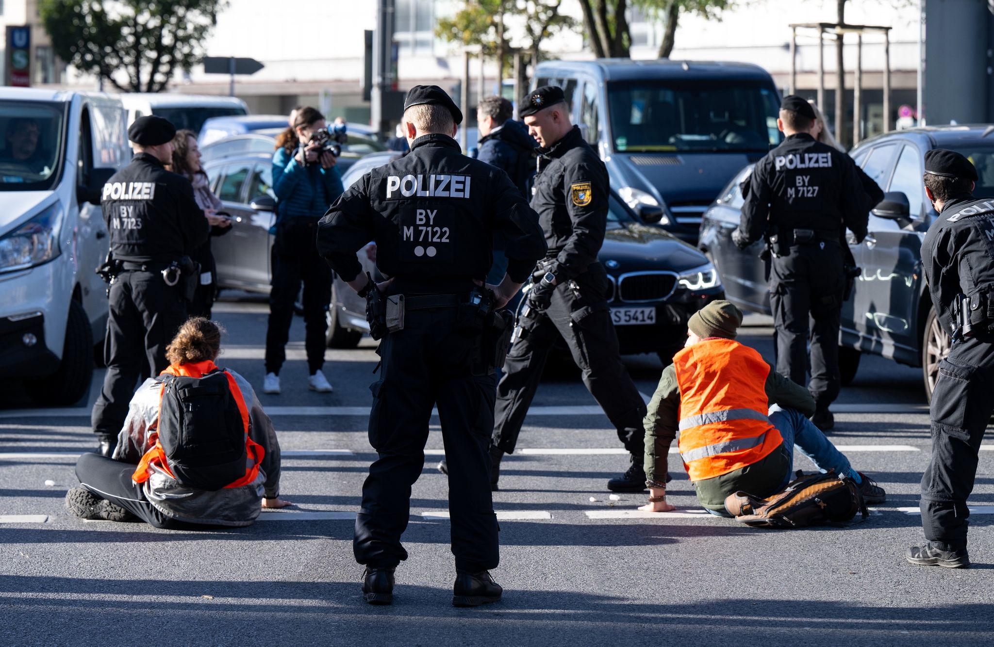 Polizeibeamte stehen neben Klimaaktivisten, die sich am Karlsplatz auf die Fahrbahn geklebt haben.