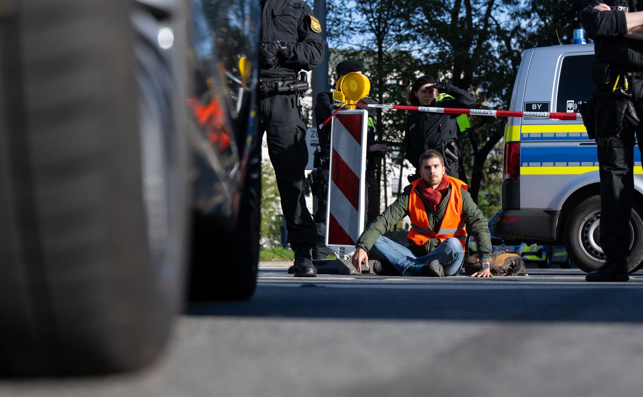 Polizeibeamte stehen neben einem Klimaaktivisten, der sich in der Münchner Innenstadt auf die Fahrbahn geklebt hat.