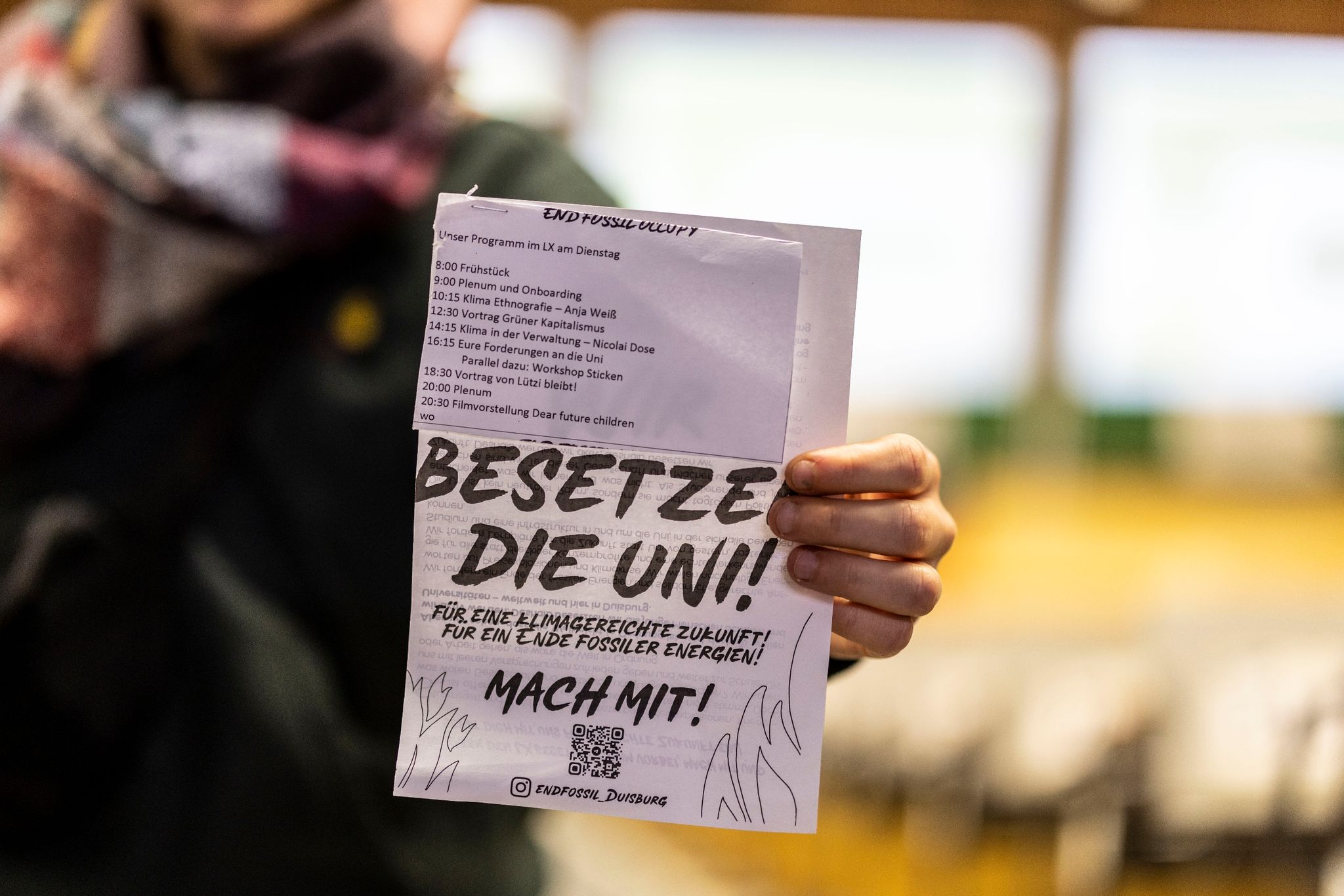 Eine Aktivistin hält einen Flyer in ihrer Hand mit der Aufschrift "Besetze die Uni!".