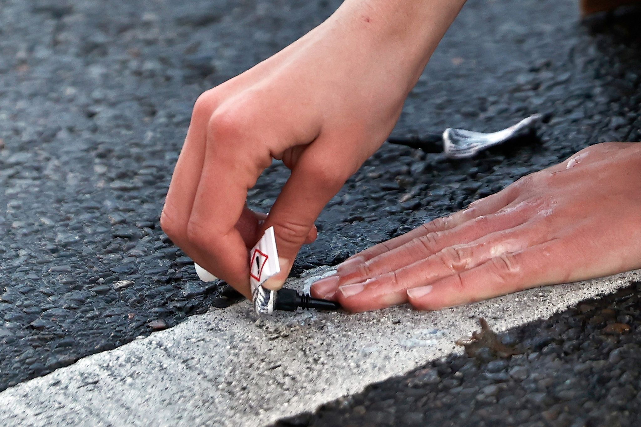Ein Aktivist klebt seine Hand mit Sekundenkleber auf der Straße fest.
