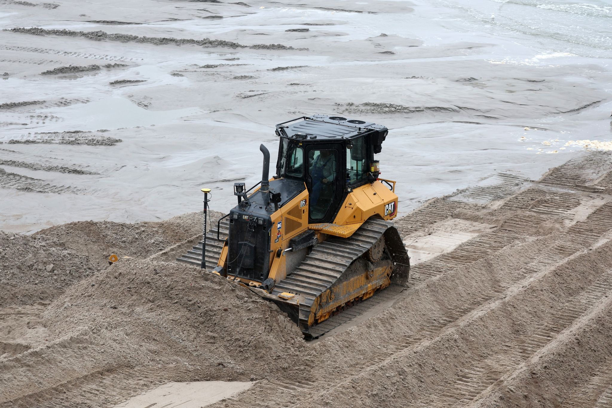 Eine Planierraupe verteilt am Ostseestrand den Sand.