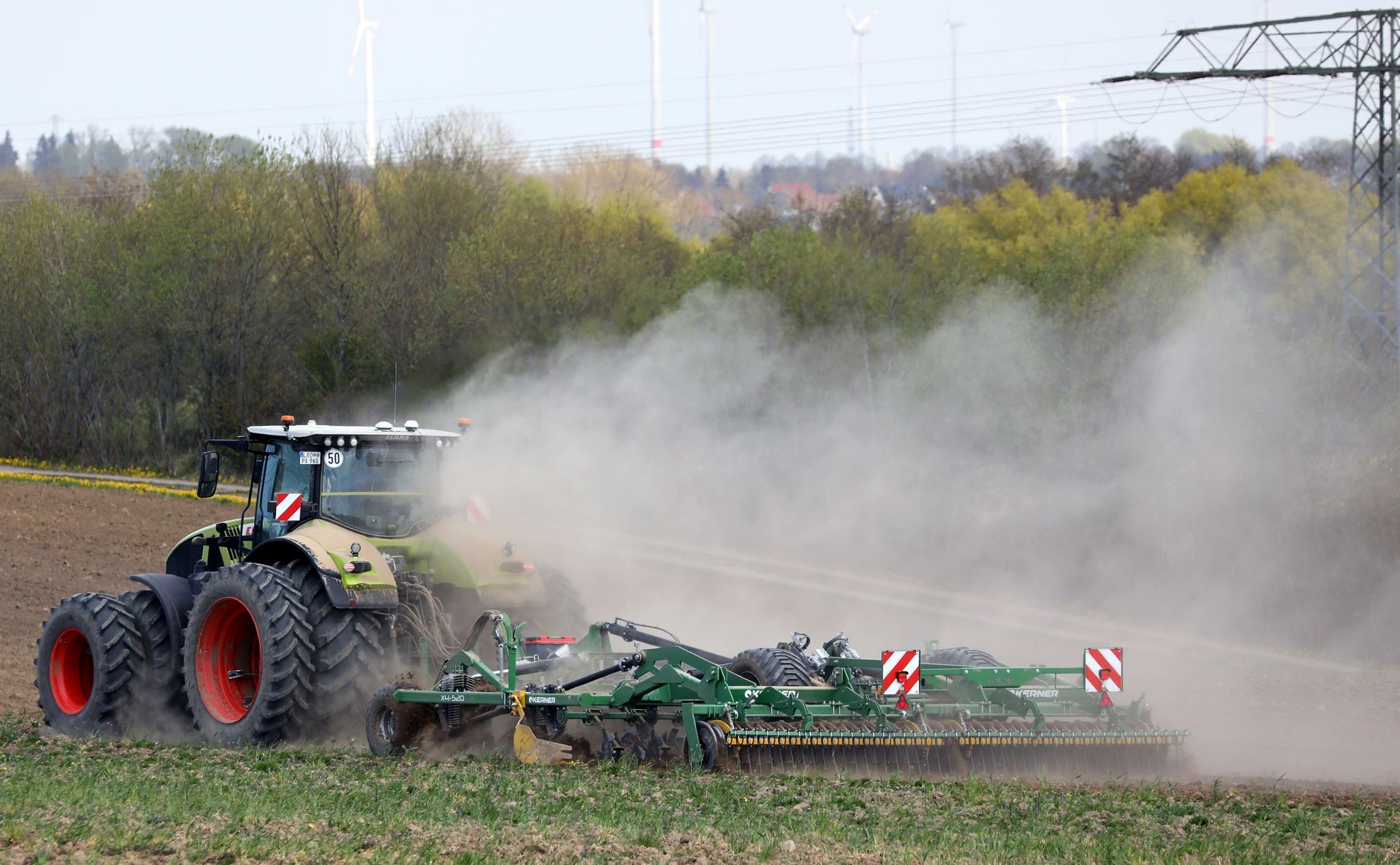 Ein Traktor zieht beim Grubbern auf einem Feld eine große Staubfahne hinter sich her.