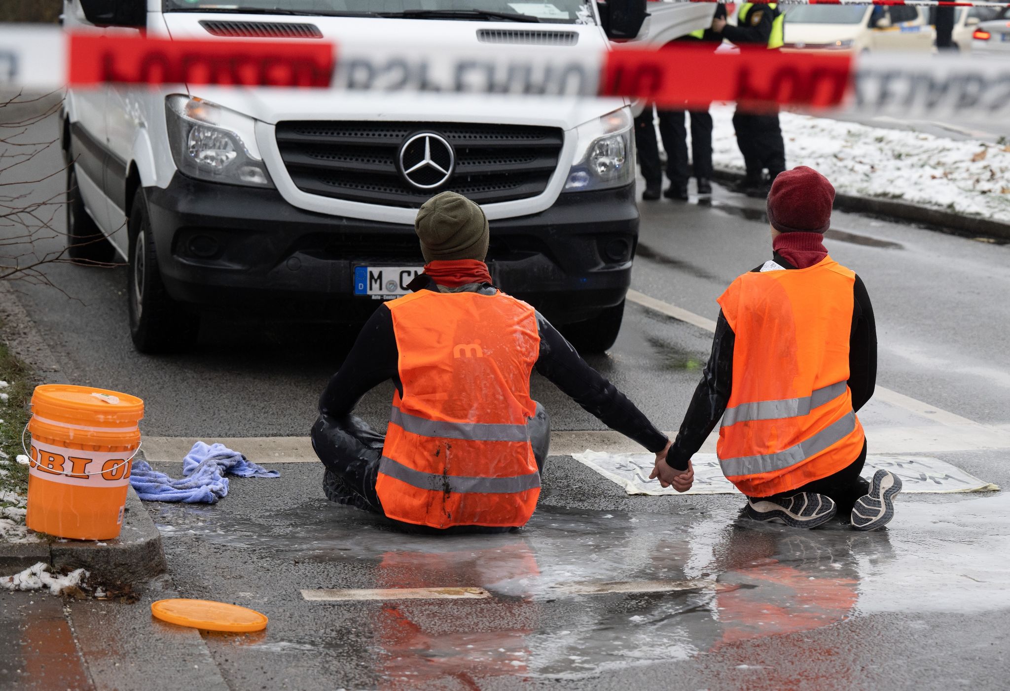 Zwei Klimaaktivisten der «Letzten Generation» versuchen, sich auf einer Straße in München trotz Nieselregen und Minusgraden festzukleben.