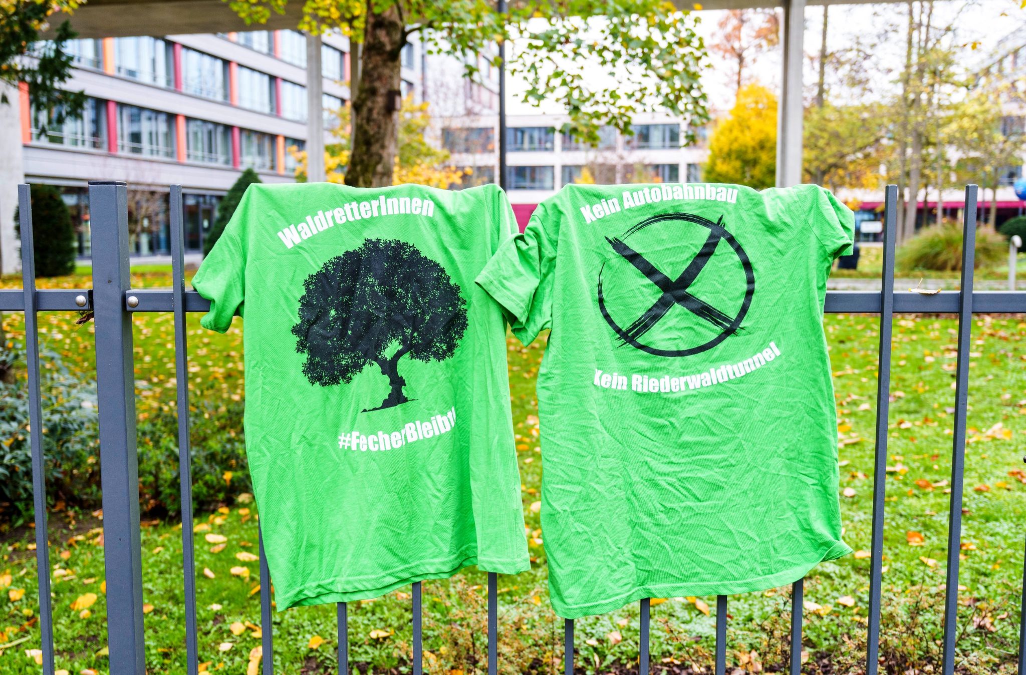 Zwei T-Shirts „Waldretterinnen ‚FecherBleibt“ und „Kein Autobahnbau Kein Riederwaldtunnel“ hängen am Zaun der Bundesbehörde.