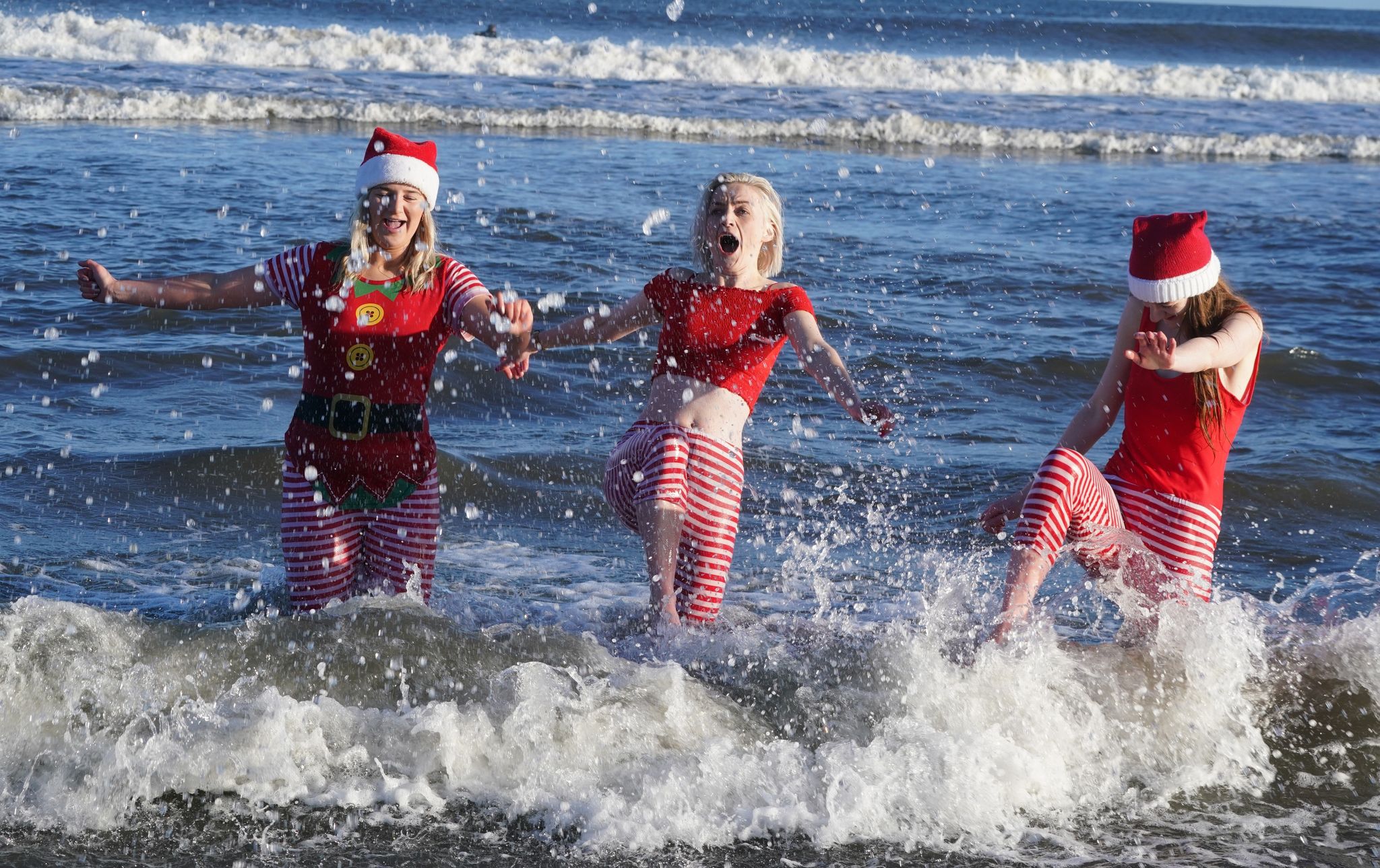 Eine Gruppe junger Frauen in Weihnachtskostümen planscht während des jährlichen Weihnachtsschwimmens am Long Sands Beach.