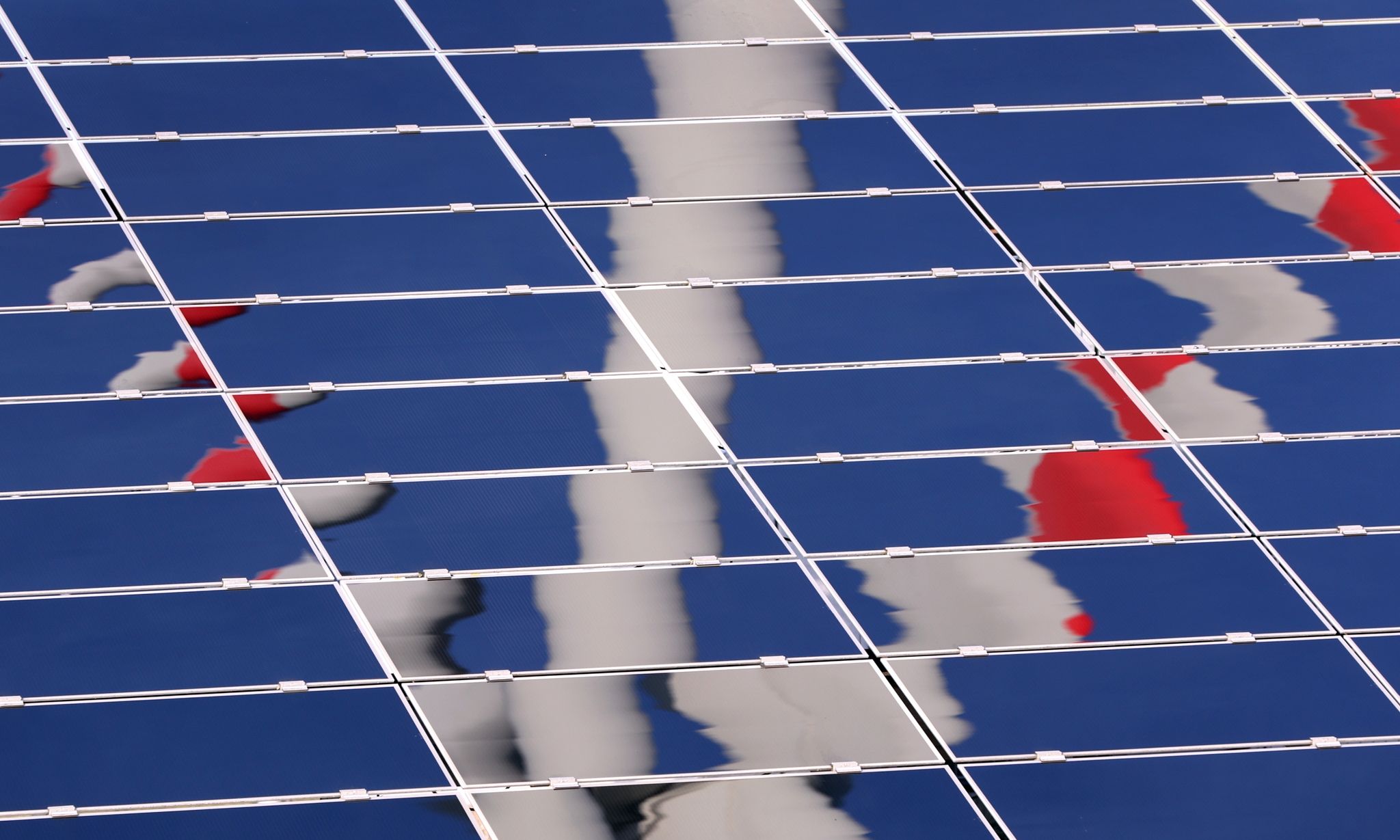 Ein Windrad spiegelt sich in eine Photovoltaik-Anlage eines Solarparks.