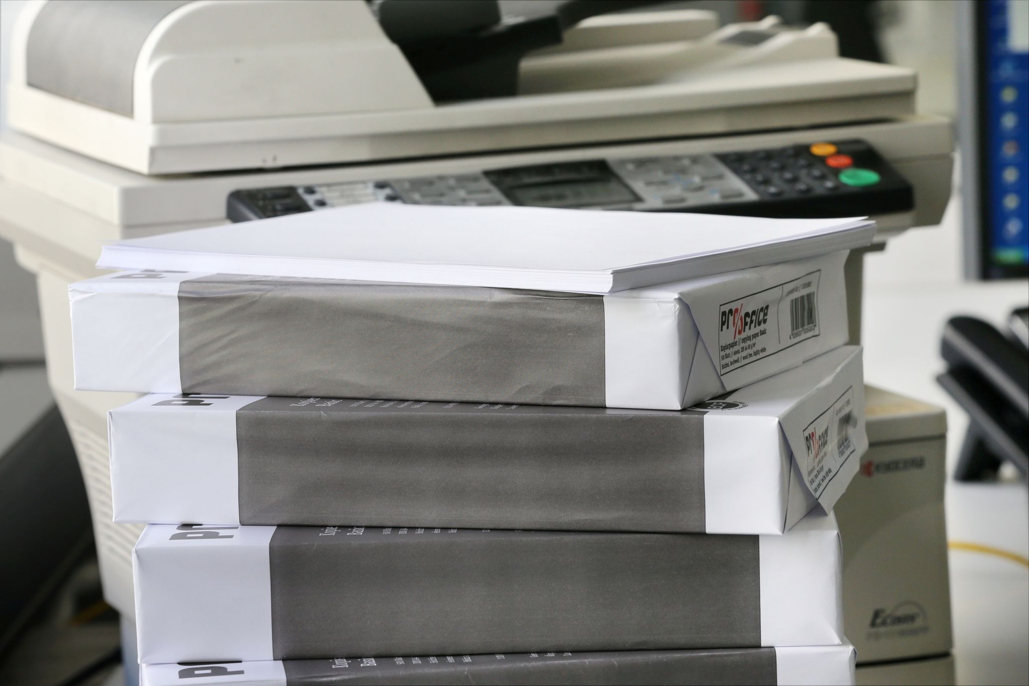 Packungen mit weißem DIN A4-Papier liegen vor einem Drucker.