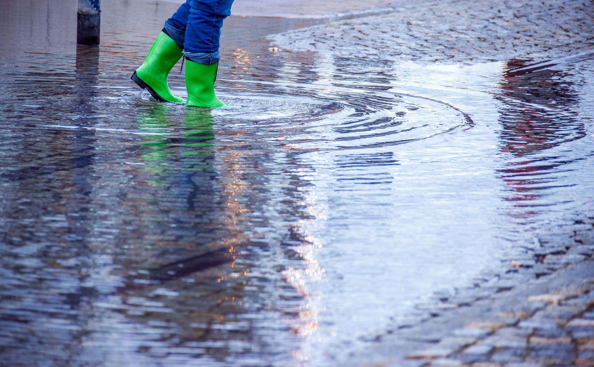 Mit Gummistiefeln geht eine Frau über eine leicht überflutete Straße.
