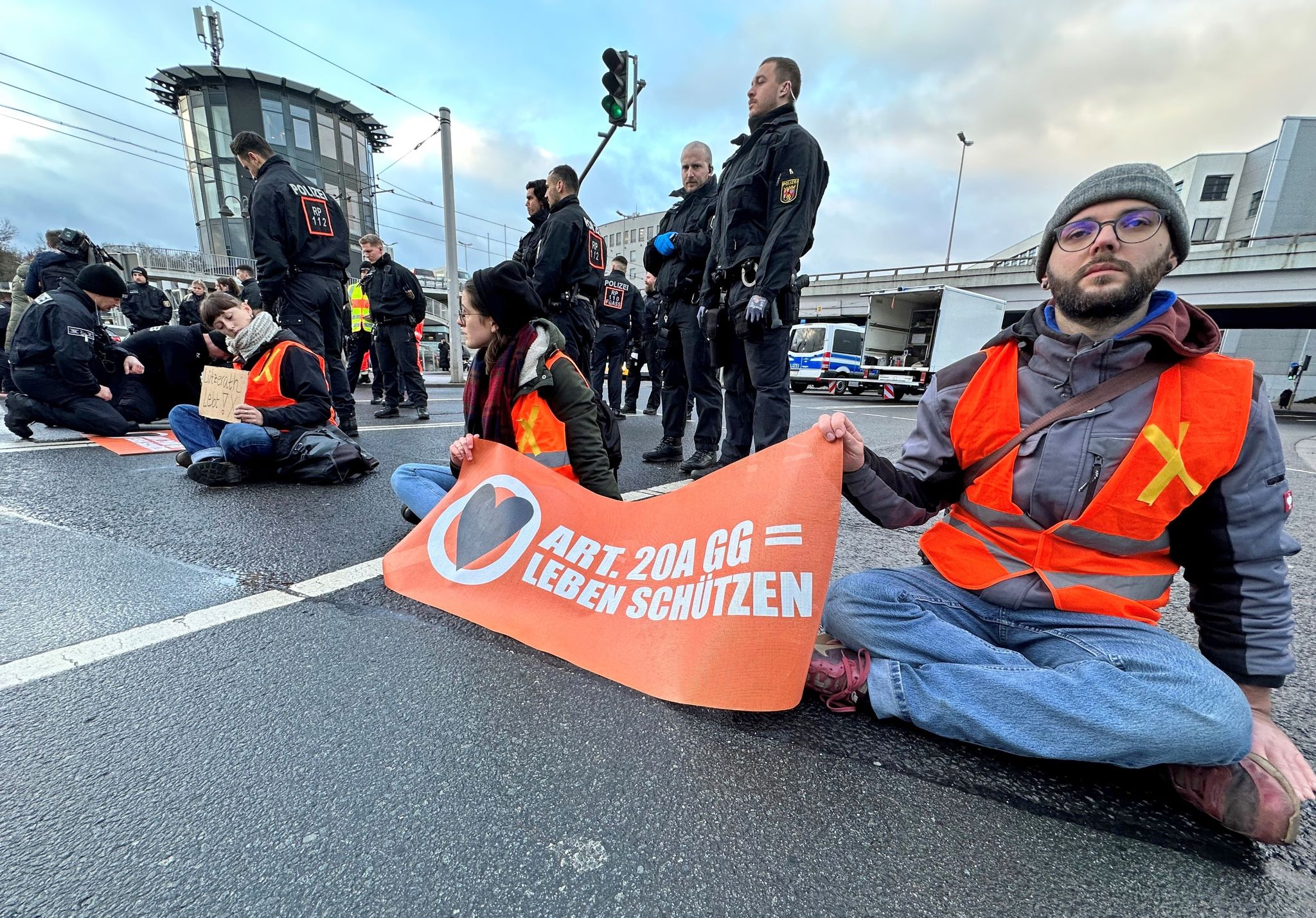 Teilnehmer einer Blockade-Aktion der Klimaschutzbewegung Letzte Generation sitzen auf einer Hauptverkehrsstraße in Mainz.