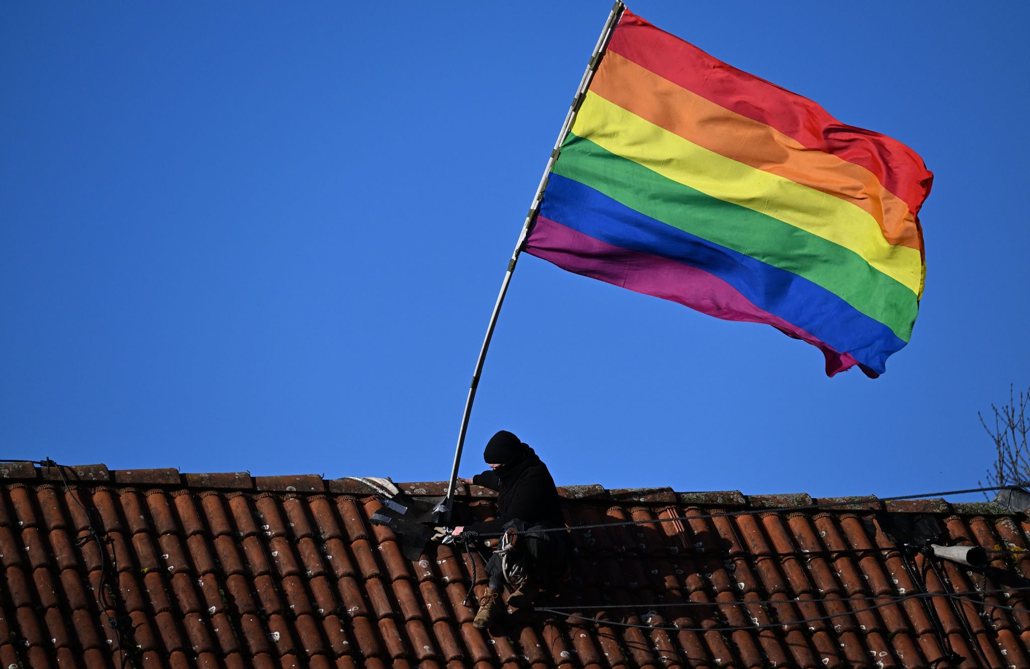 Ein Aktivist montiert während der Räumung von Lützerath eine Regenbogenfahne auf einem Dach.