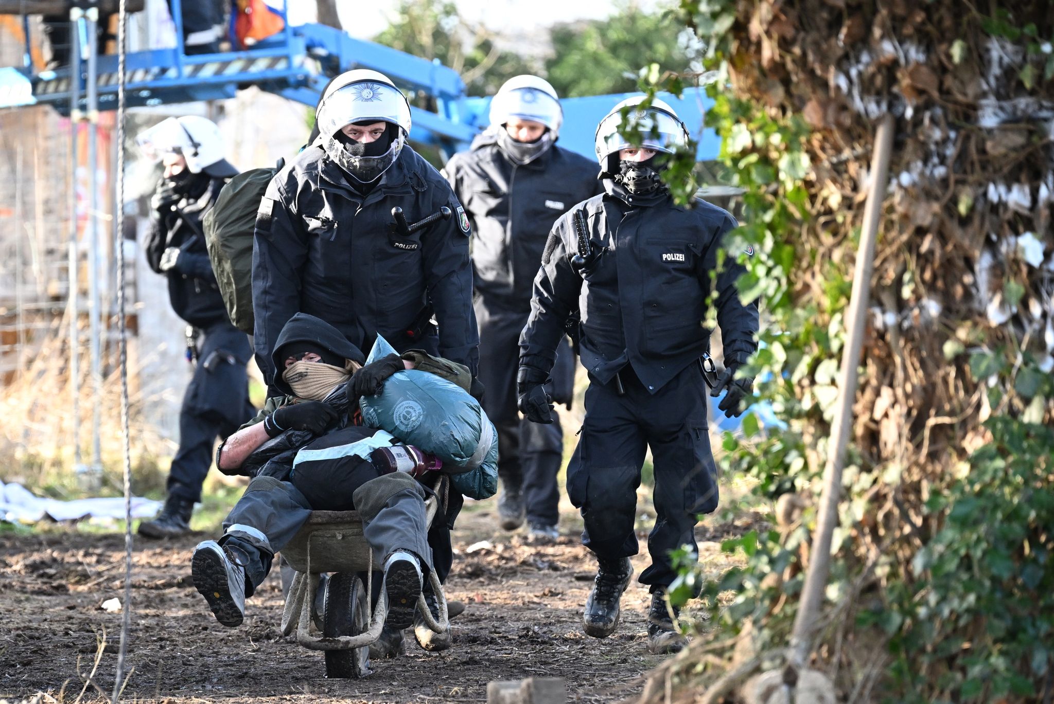 Polizisten schieben einen Klimaaktivisten mit der Schubkarre vom Gelände in Lützerath.