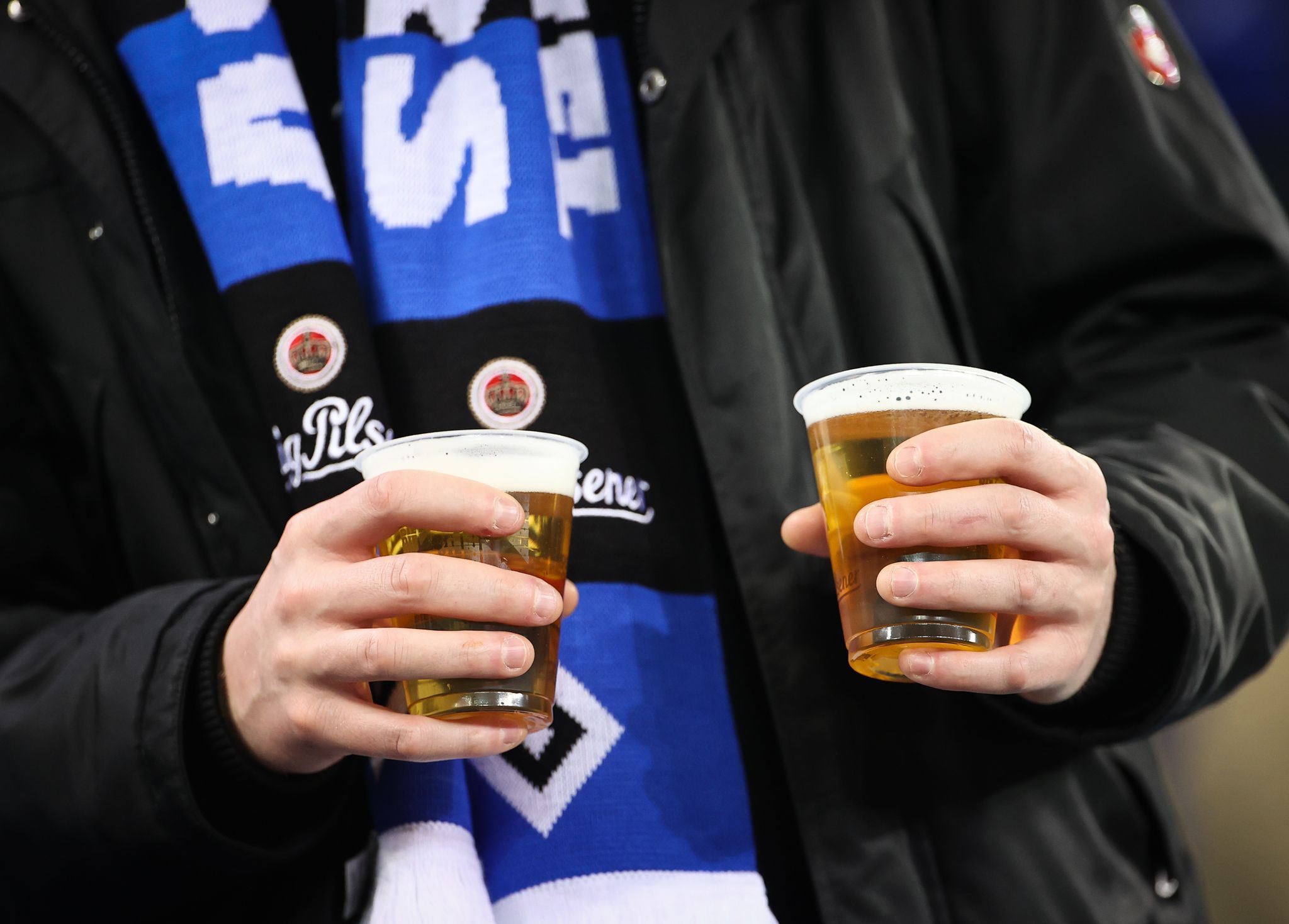 Ein Fußballfan des Hamburger SV trägt zwei Einwegbecher mit Bier auf der Tribüne.