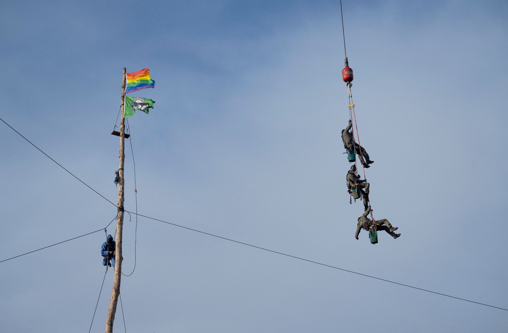 Am Seil eines Kranes werden Polizisten zu einem Besetzer geschwenkt, der in 30 Metern Höhe hängt.