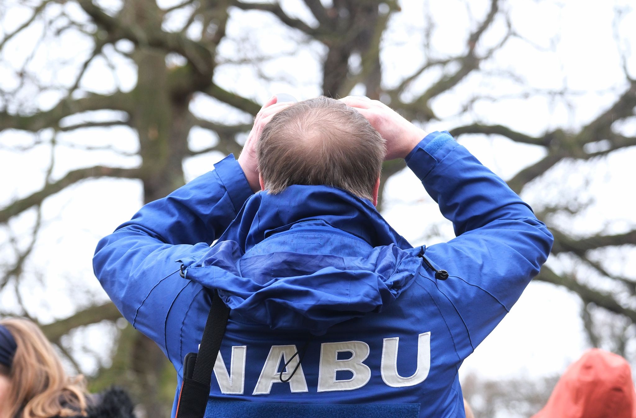 Ein Mann mit einer Jacke des Naturschutzbunds Deutschland (NABU) blickt durch ein Fernglas.
