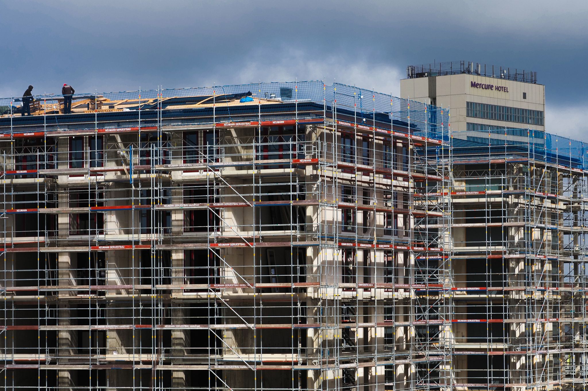 Arbeiter stehen auf dem Dach eines Rohbaus. Der Bundesverband deutscher Wohnungs- und Immobilienunternehmen benötigt mehr Geld für den klimagerechten Neubau.