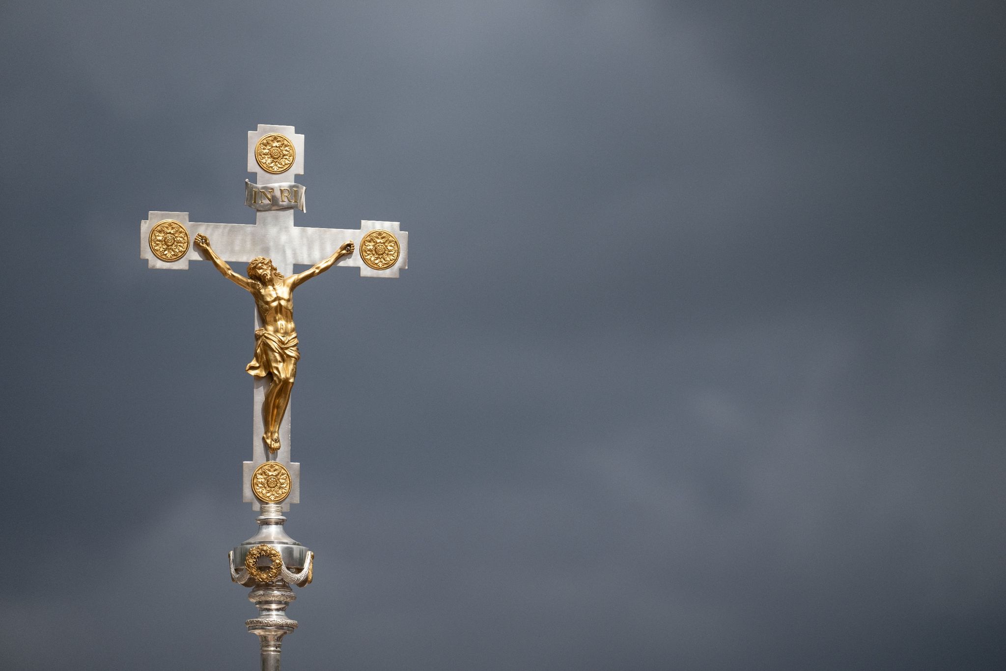 Ein katholisches Kruzifix ist vor dunklen Wolken zu sehen.