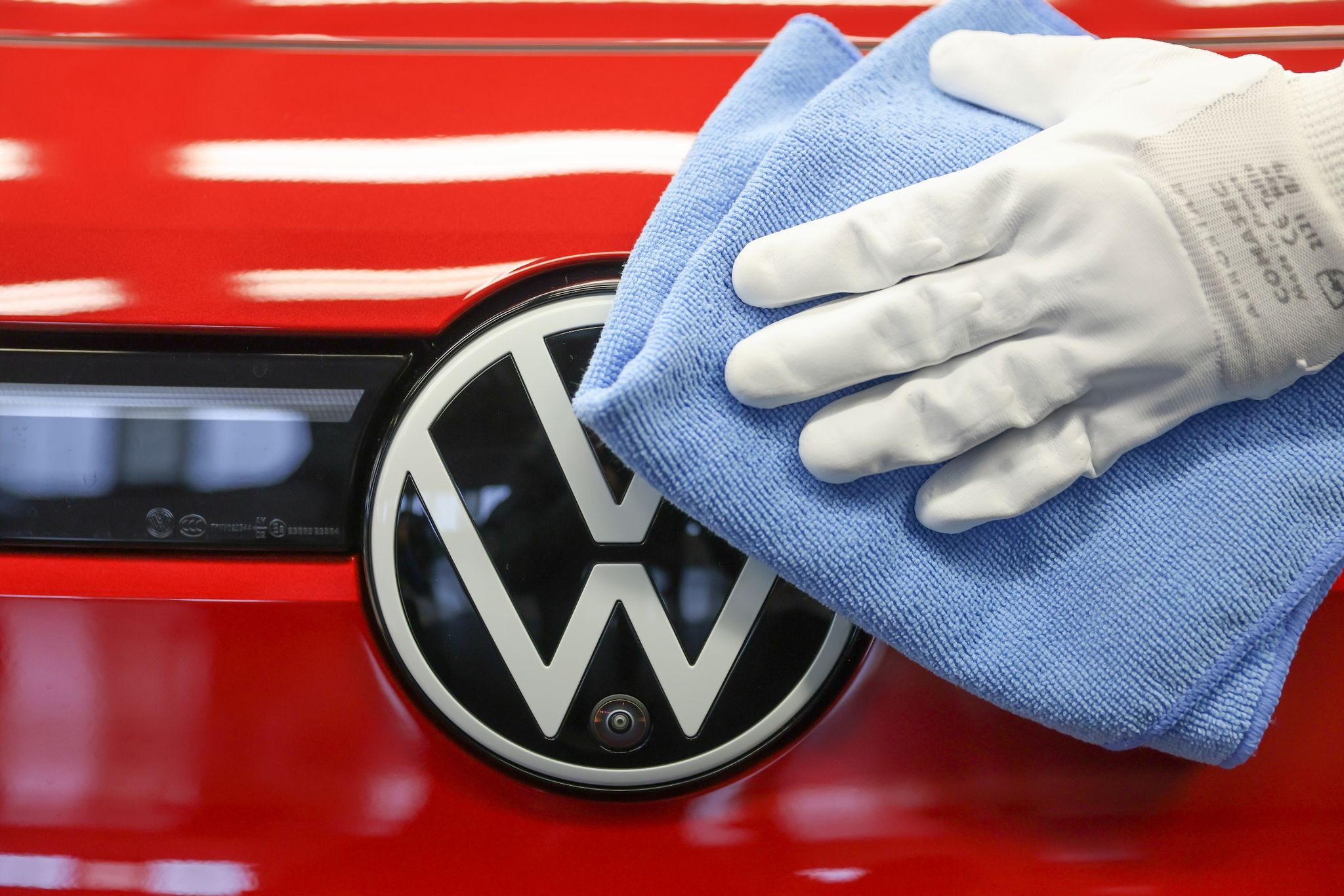 Eine Mitarbeiterin wischt über das VW-Logo an einem Auto.