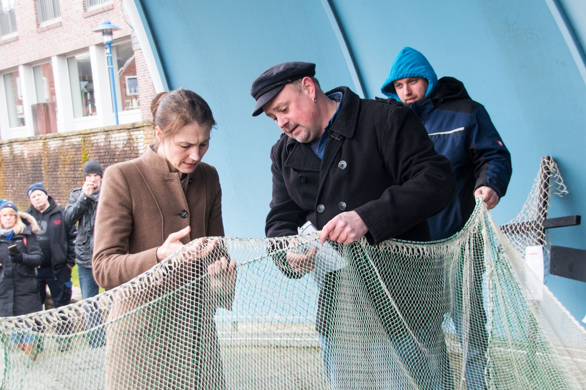 Fischer Nils Sander (M) zeigt Miriam Staudte (Bündnis 90/Die Grünen, l), Landwirtschaftsministerin von Niedersachsen, nach einem Treffen im Hafen Maschengrößen eines Netzes.