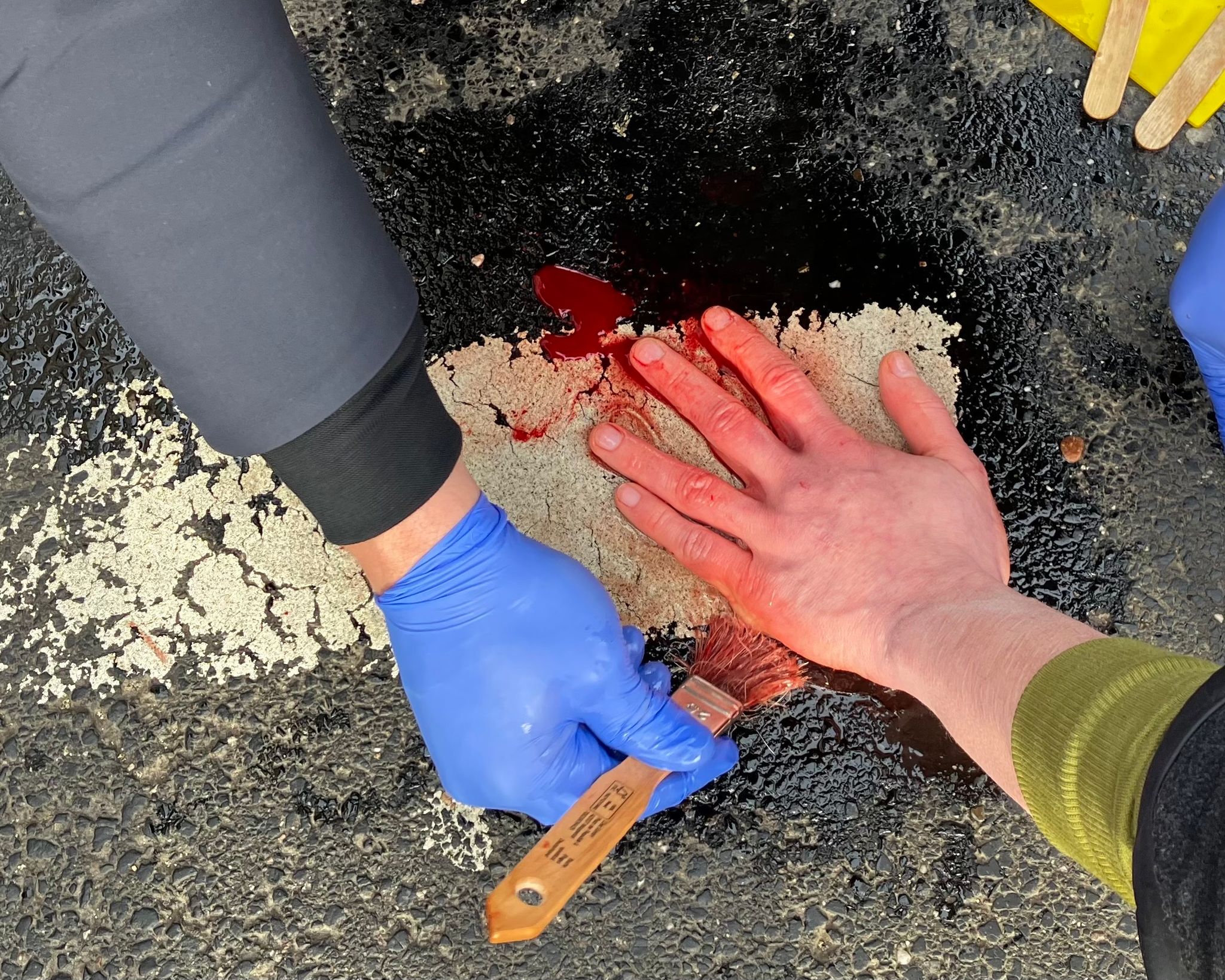 Die Hand eines Klima-Aktivisten wird vom Asphalt einer Straße in Köln mit Öl gelöst.