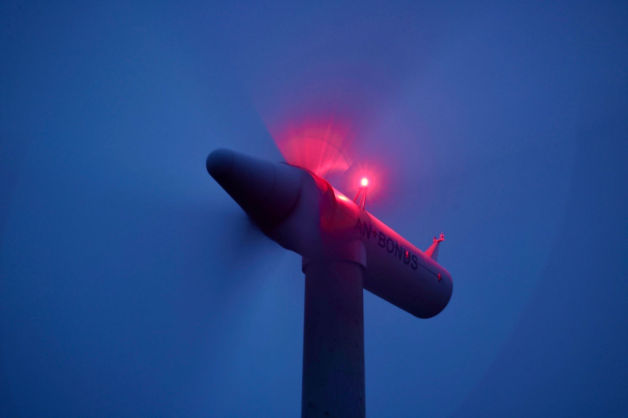 Die Rotoren einer beleuchteten Windkraftanlage drehen sich vor Sonnenaufgang.