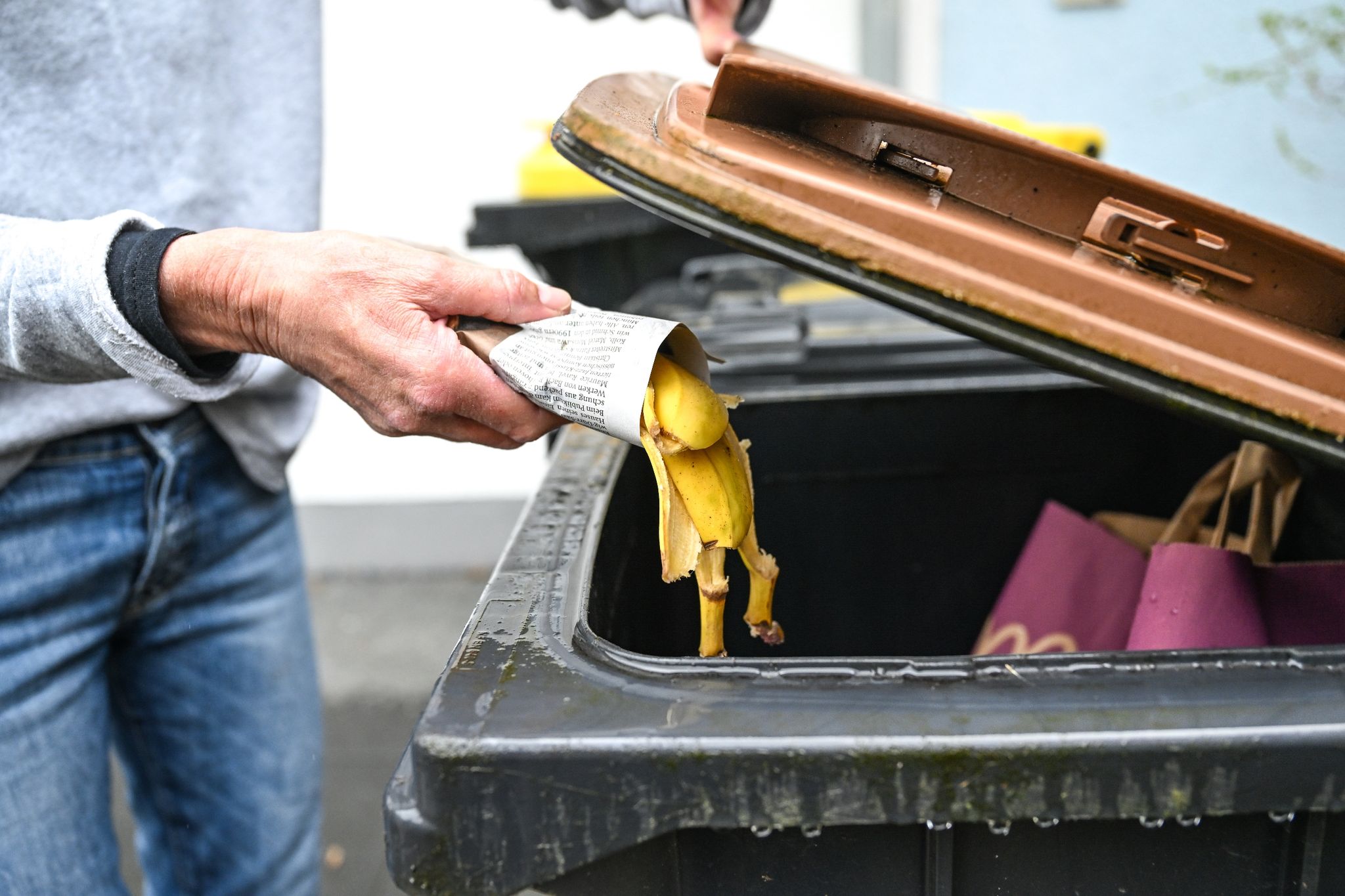 Eine Frau wirft in Zeitungspapier gewickelte Bananenschalen in eine Mülltonne für den Biomüll.