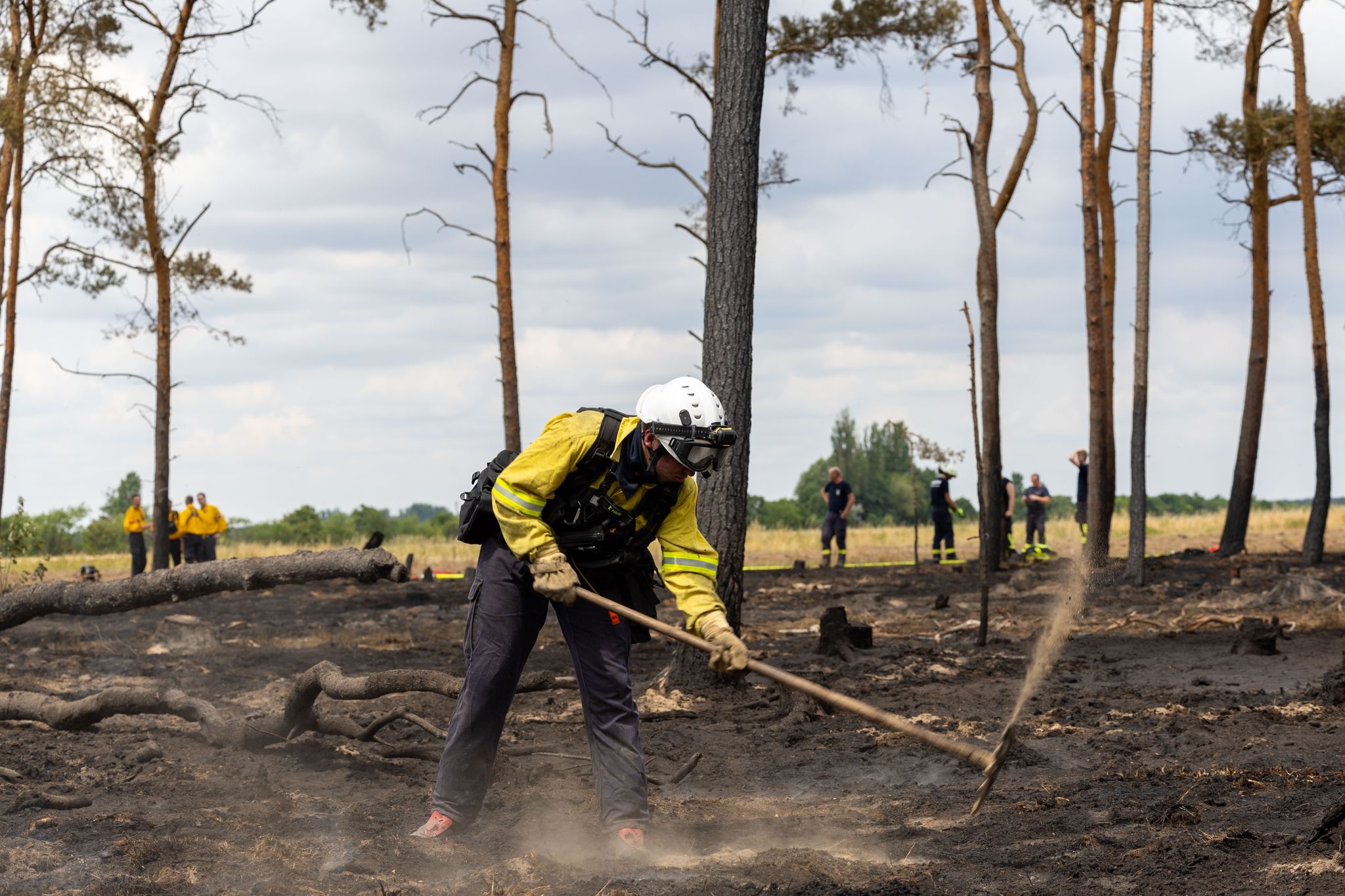 Ein Feuerwehrmann bearbeitet nach einem Waldbrand den Waldboden mit einer Hacke.
