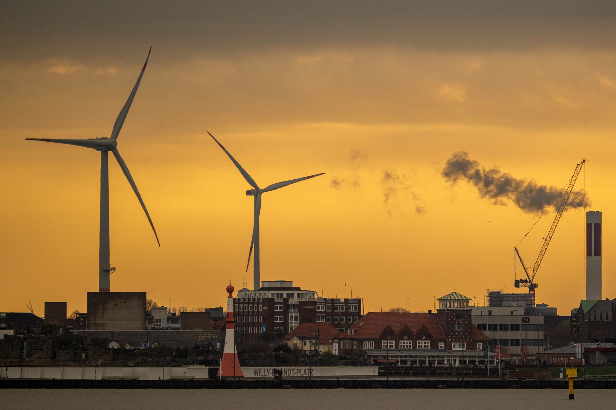 Zwei Windräder zeichnen sich vor dem morgendlichen Himmel in Bremerhaven ab.