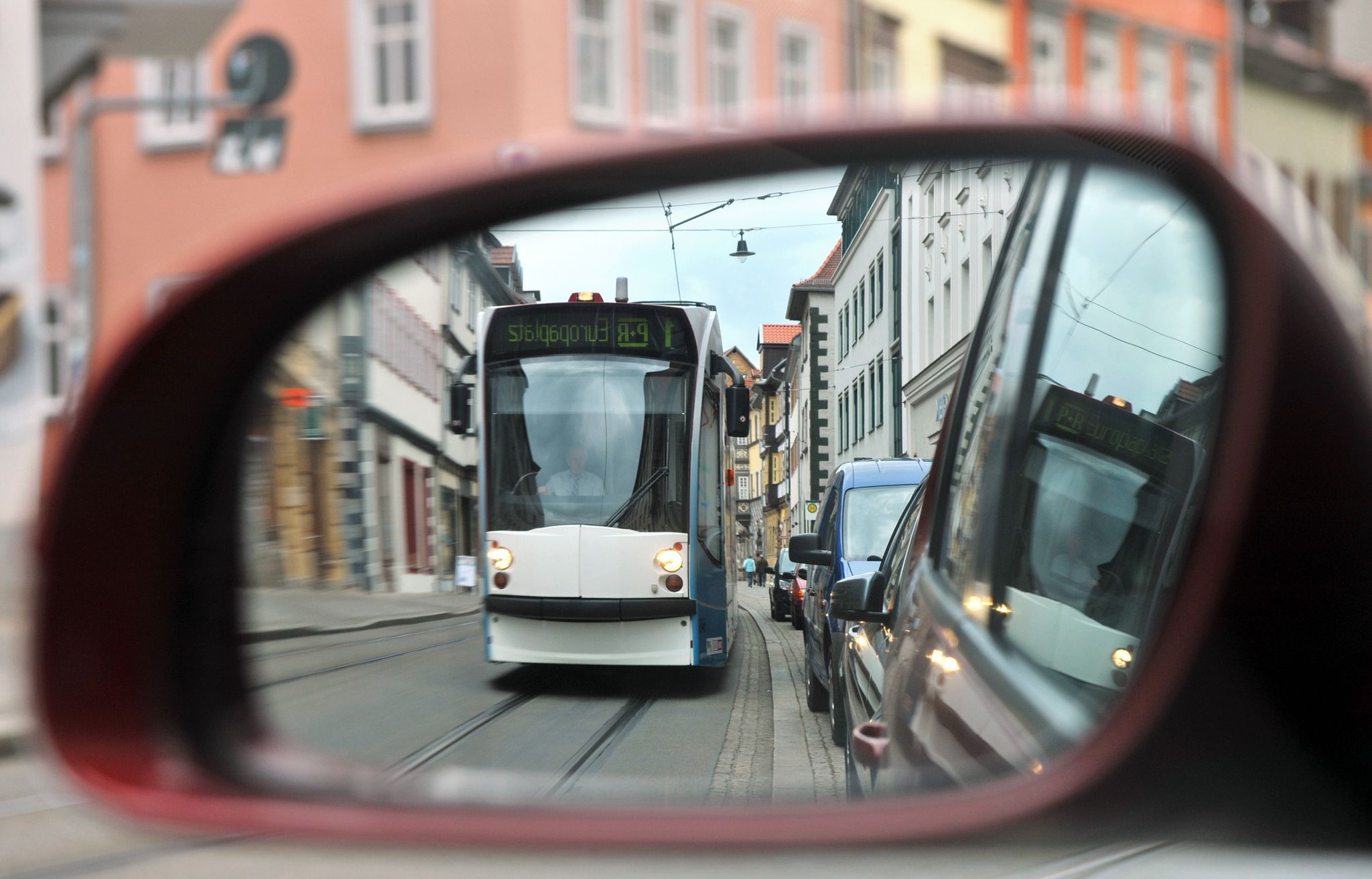 Eine Straßenbahn fährt in Erfurt die Johannesstraße entlang und spiegelt sich in einem Autospiegel.