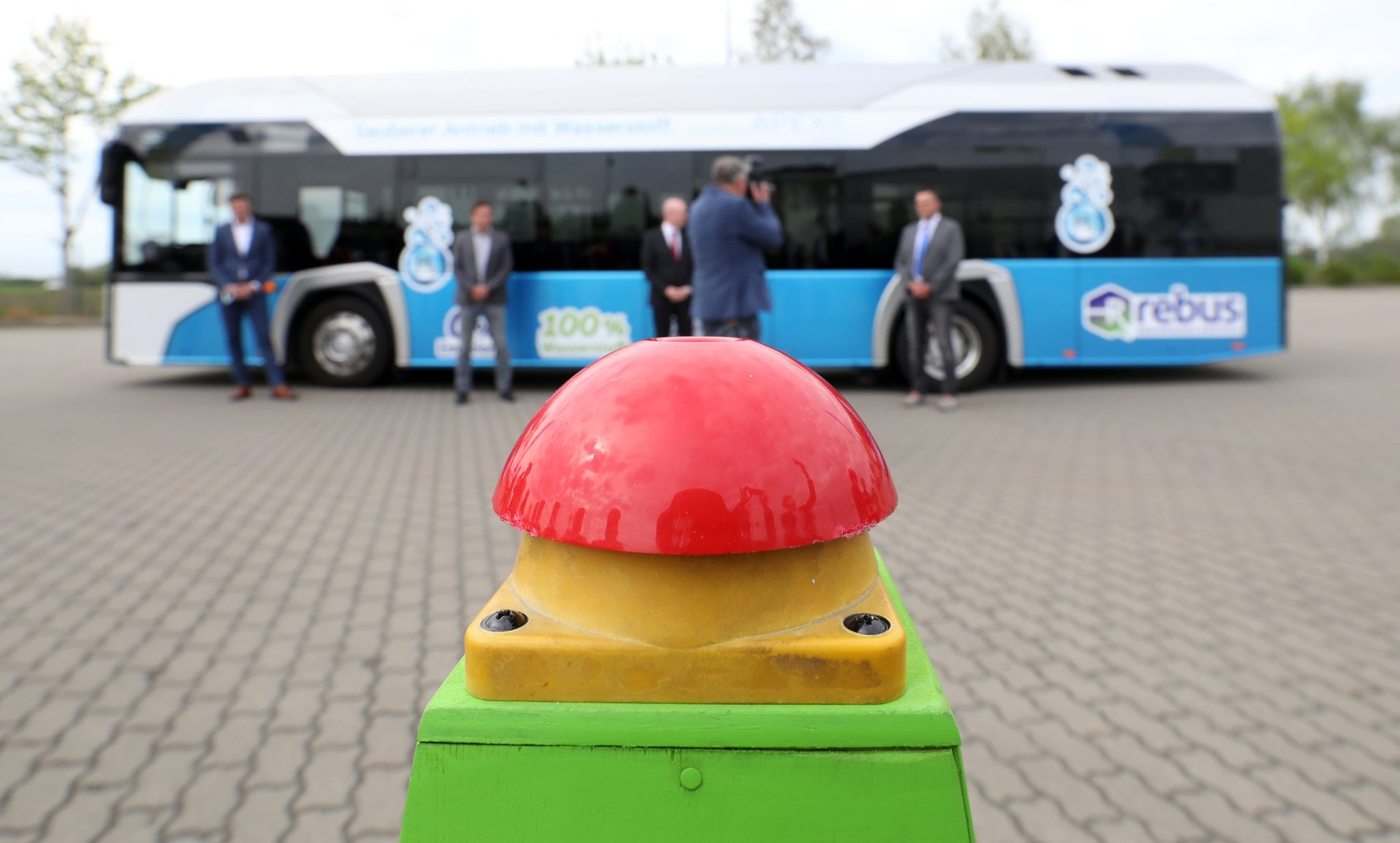 Der erste Wasserstoffbus in Mecklenburg-Vorpommern wird vorgestellt, ein roter Buzzer zur offiziellen Inbetriebnahme steht im Vordergrund bereit.