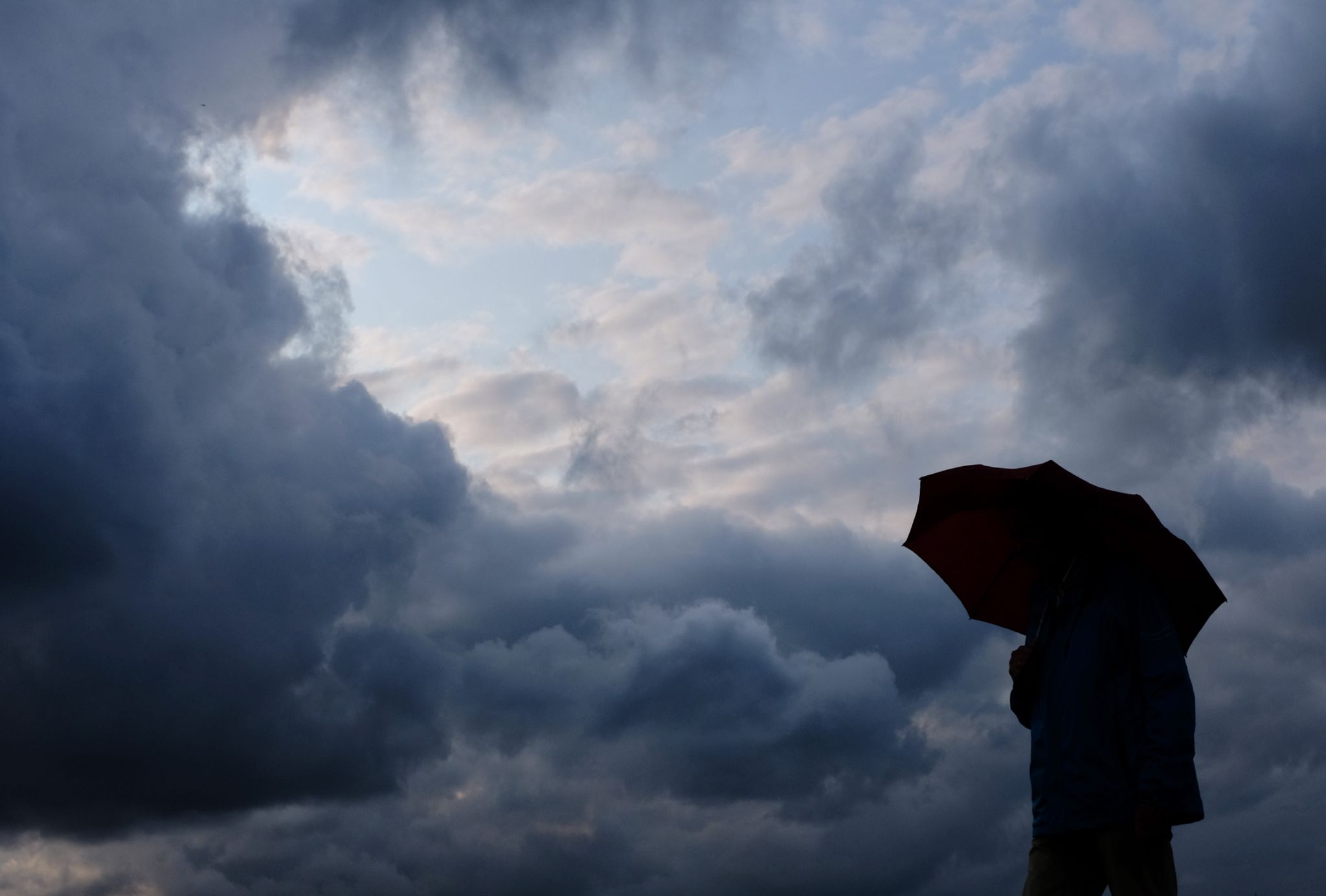Ein Mann geht mit einem Regenschirm vor aufziehenden dunklen Wolken in Duisburg spazieren. (Symbolbild)