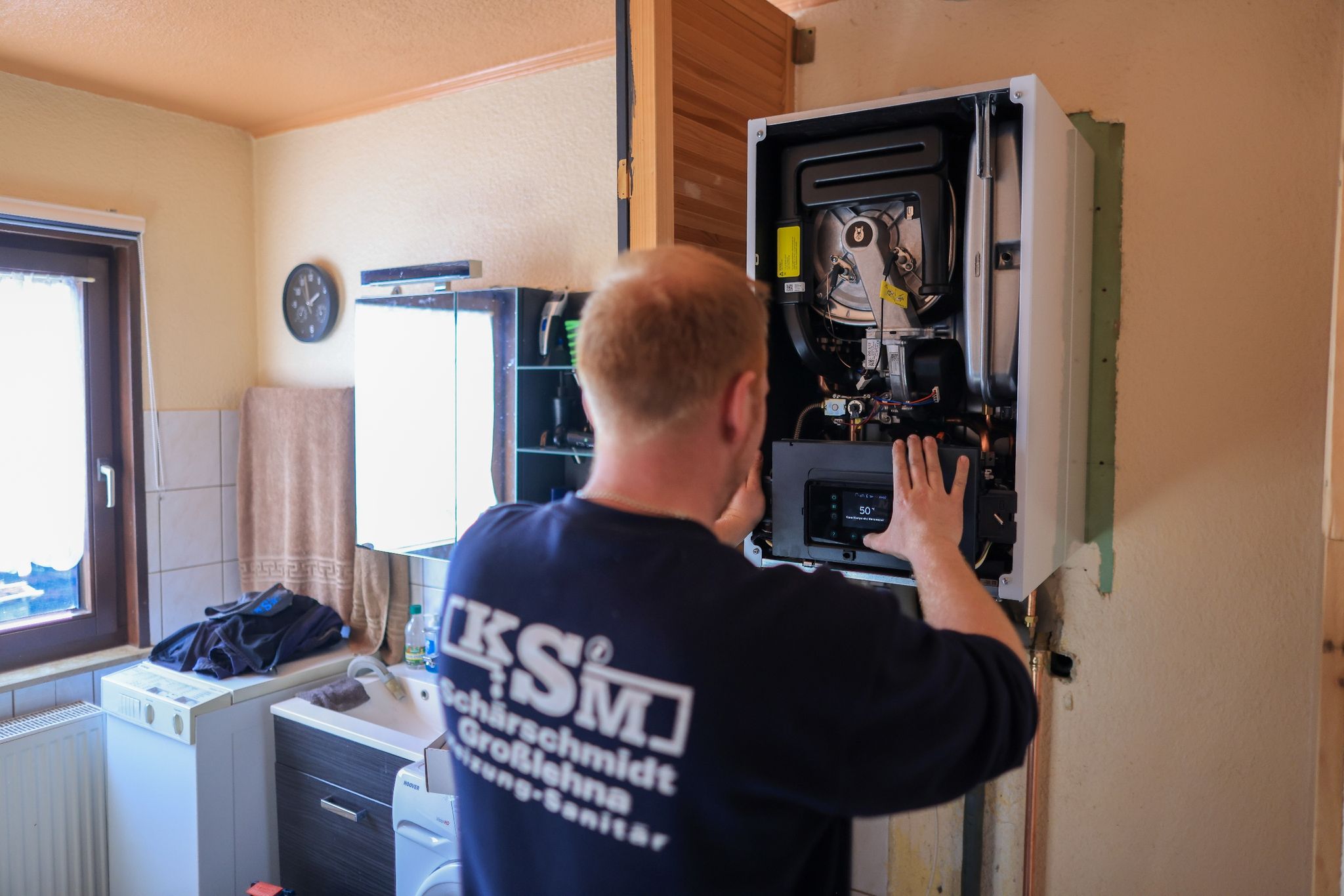 Der Mitarbeiter einer Sanitär- und Heizungsbaufirma installiert in einem Einfamilienhaus eine moderne Gasbrennwerttherme.