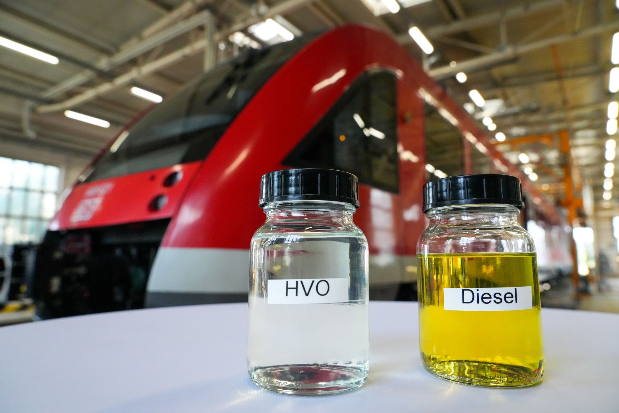 Ein Glas mit Diesel (r) und eins mit Hydrotreated Vegetable Oil (HVO) stehen vor einem Regionalzug auf einem Tisch.