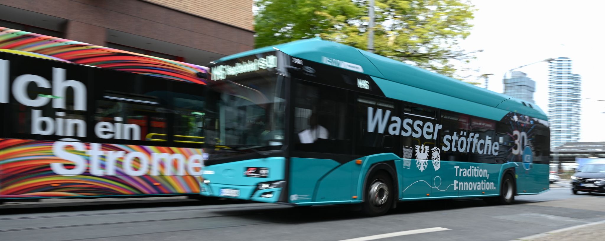 Ein Wasserstoff-Bus der Linie M46 mit der Aufschrift "Wasserstöffche" fährt am Hauptbahnhof an einem E-Bus vorbei.