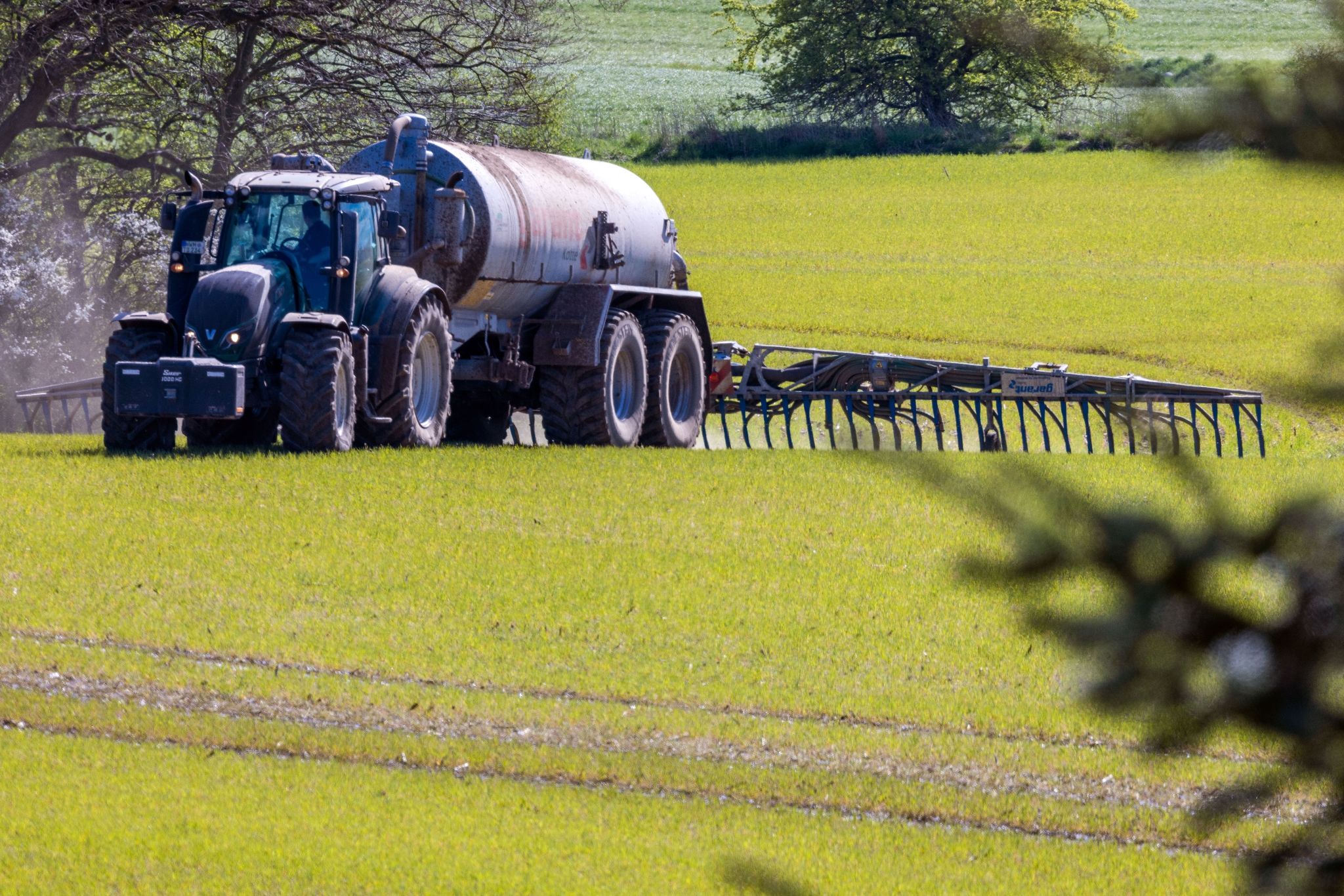 Ein Traktor zieht einen Tankwagen über ein Feld und verteilt Gülle im Boden.