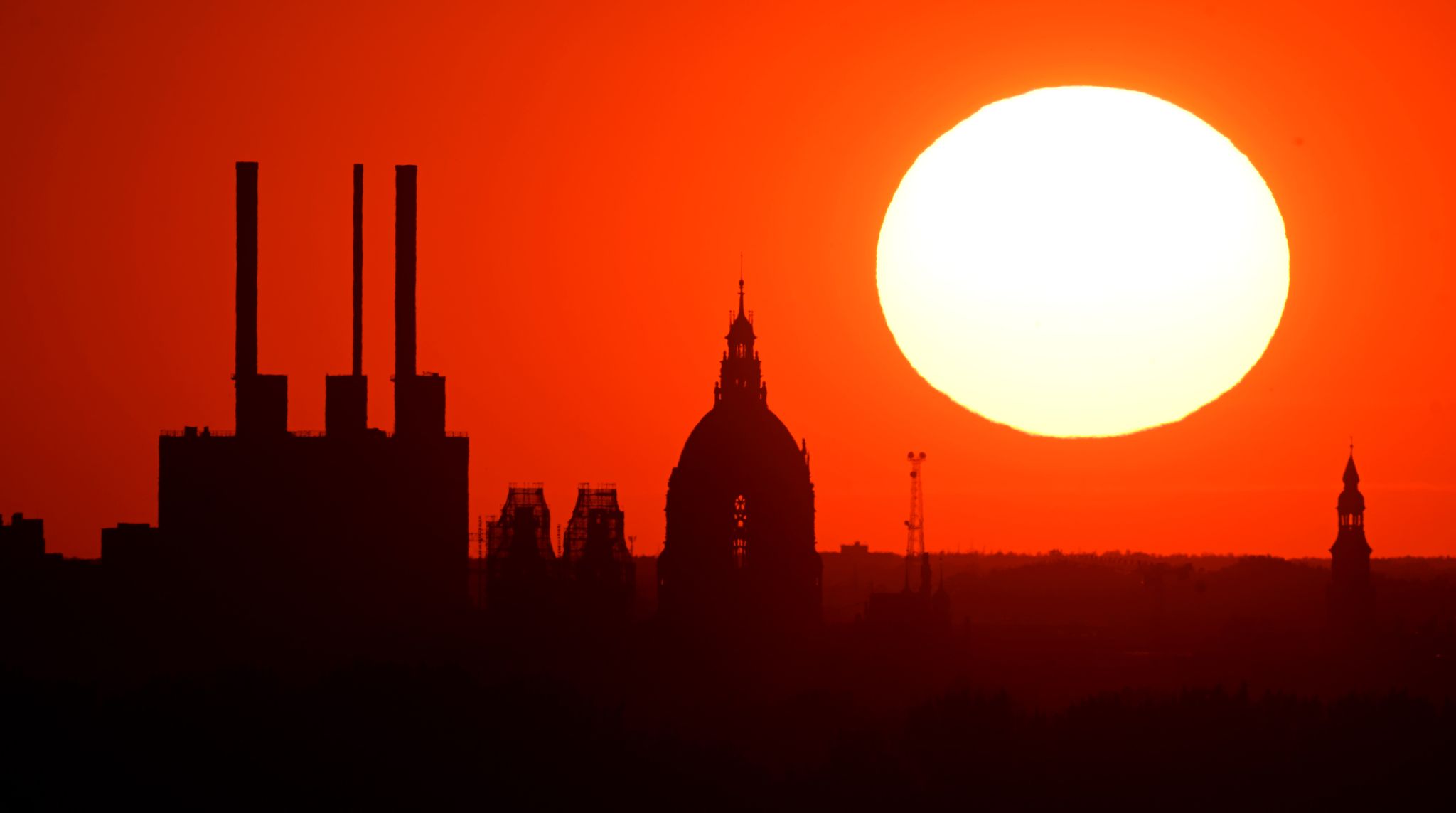 Die Sonne geht hinter dem Gaskraftwerk Linden und dem Neuen Rathaus unter.
