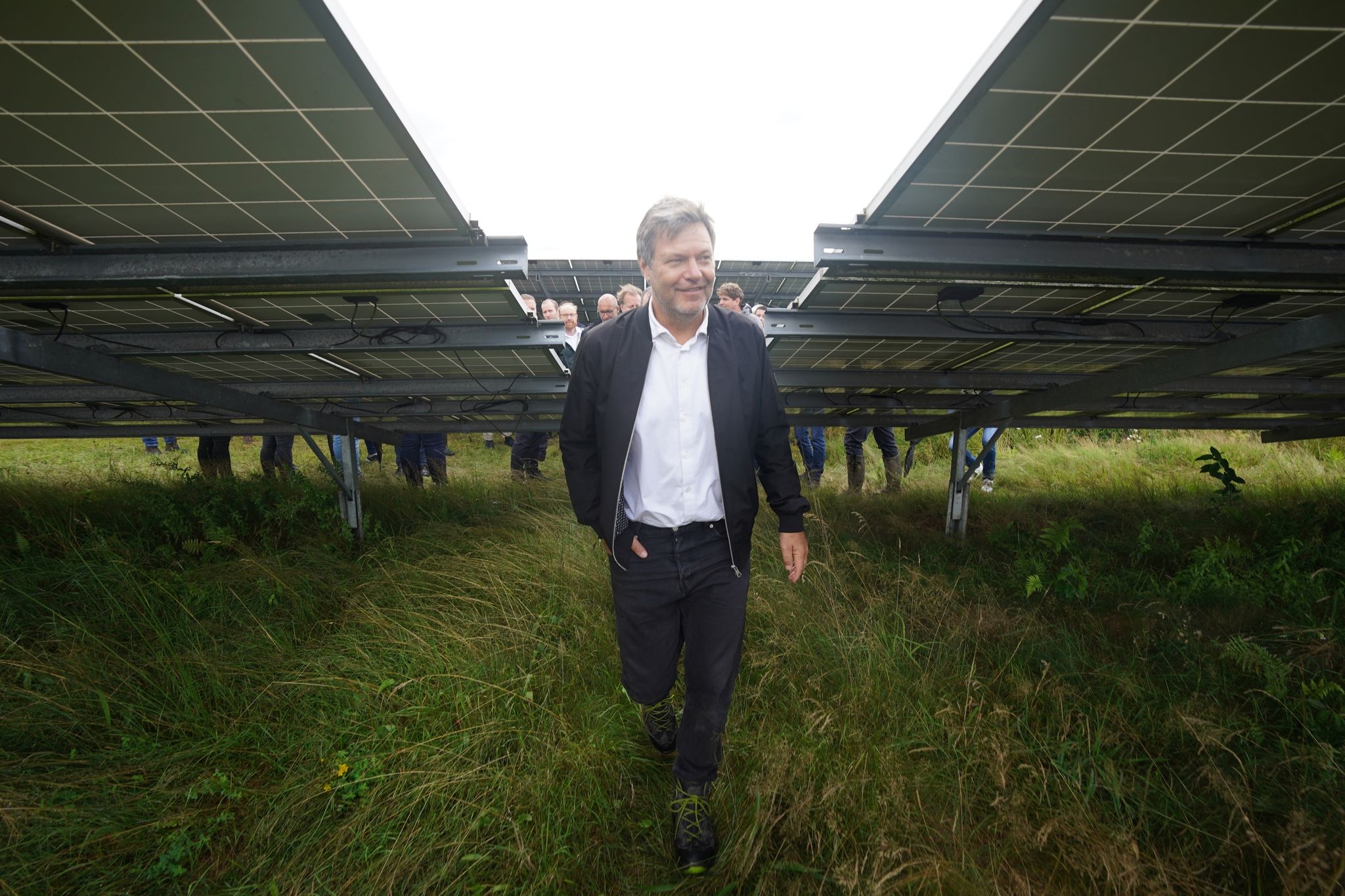 Robert Habeck geht zwischen Solarmodulen im Solarpark Klein Rheide hindurch.