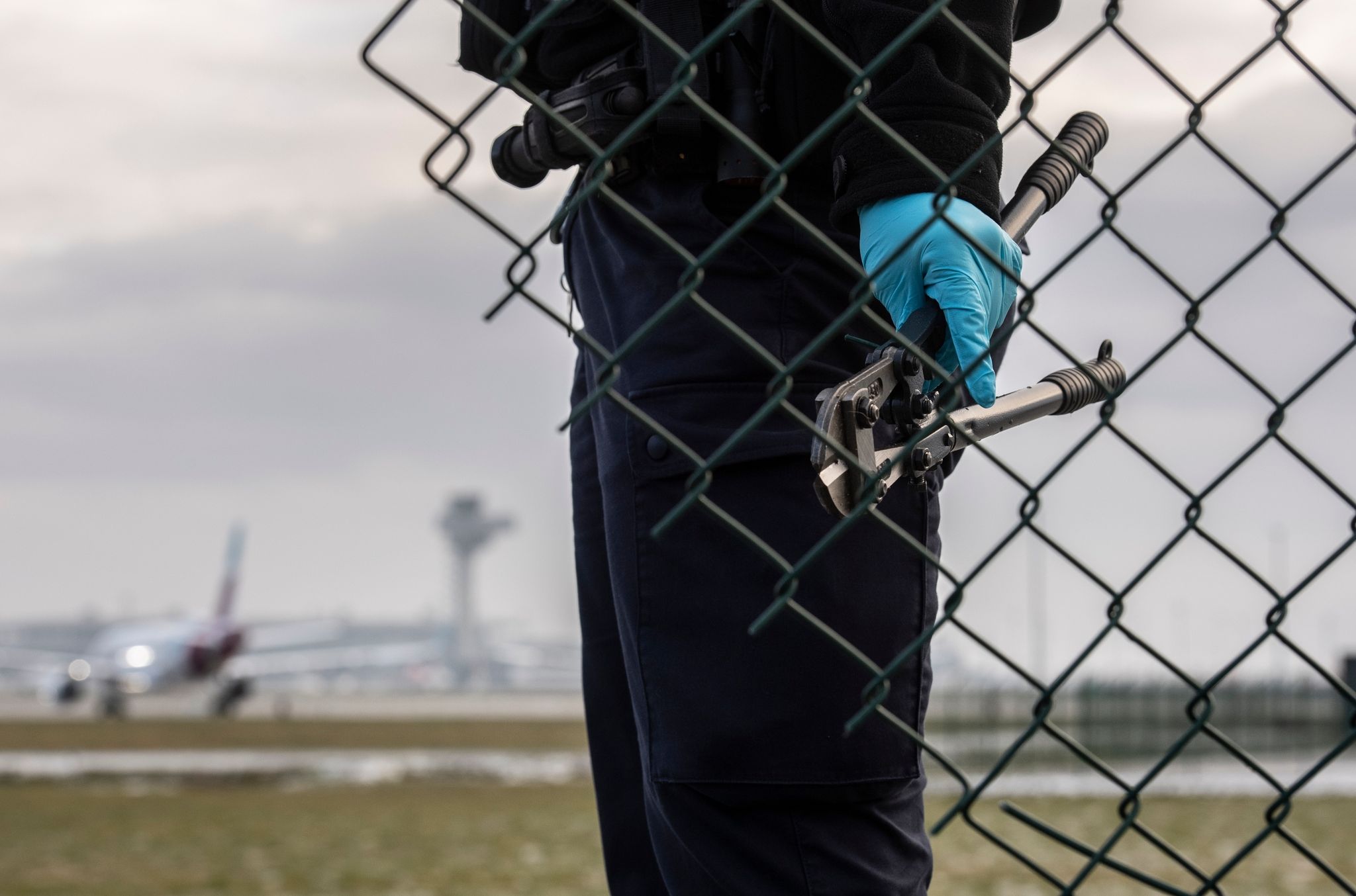Eine Beamtin der Bundespolizei steht mit einem sichergestellten Bolzenschneider an einem Zaun am BER-Flughafen.