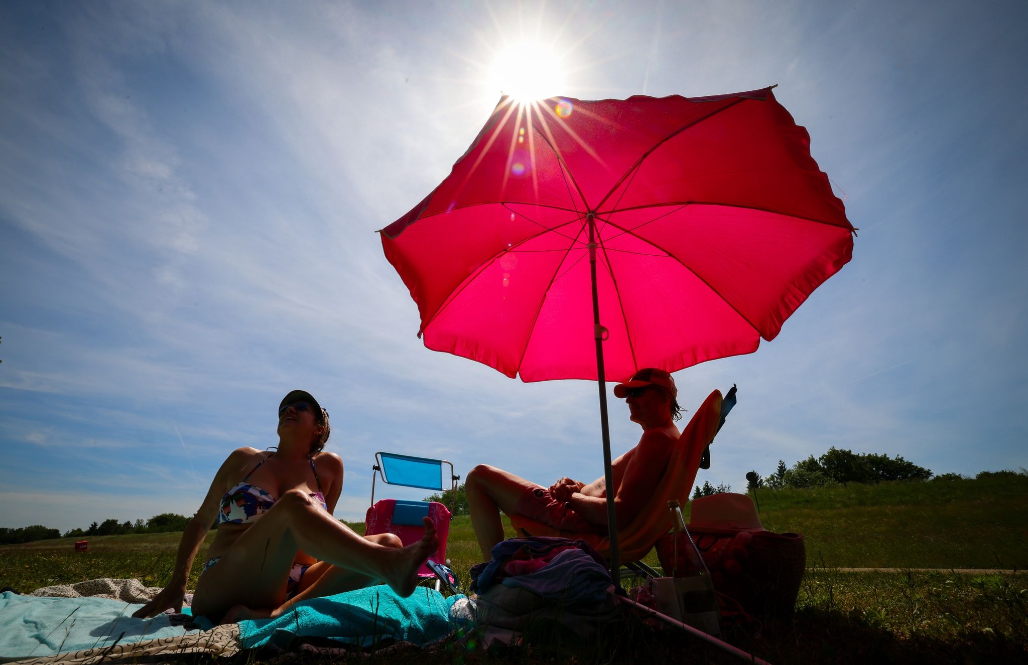 Unter einem pinkfarbenen Sonnenschirm genießen zwei Menschen den sonnigen Tag.
