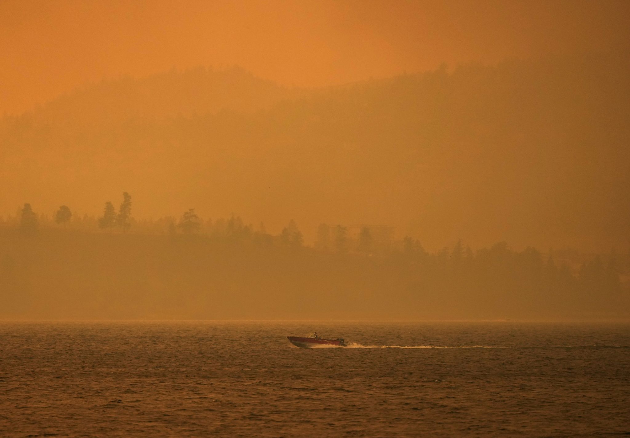 Ein Boot fährt auf dem Okanagan-See, während der Rauch des McDougall-Creek-Wildfeuers über dem Gebiet liegt.