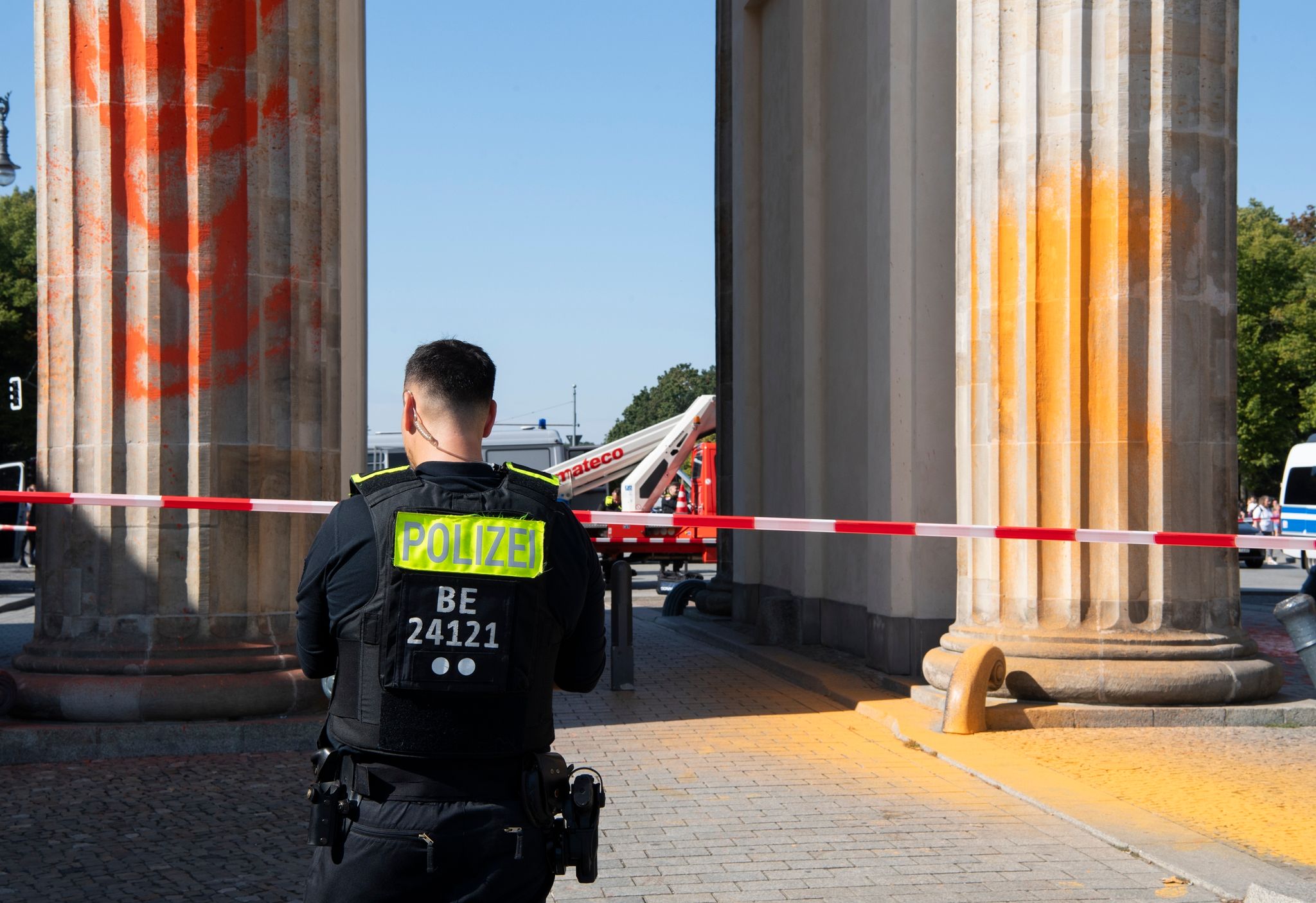 Polizisten stehen am Brandenburger Tor, das Mitglieder der Klimaschutzgruppe Letzte Generation am Sonntagvormittag mit oranger Farbe angesprüht haben.
