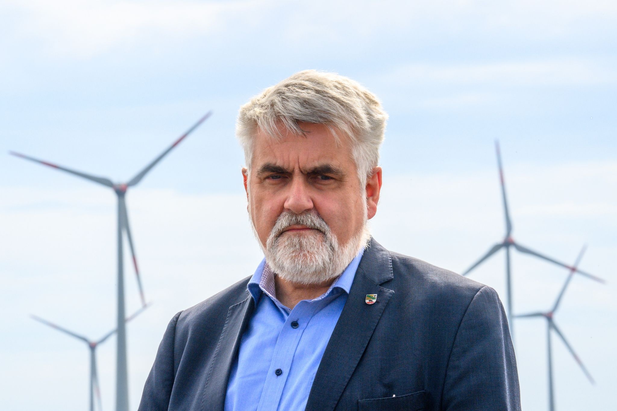 Armin Willingmann (SPD) steht in einem Windpark vor Windrädern.