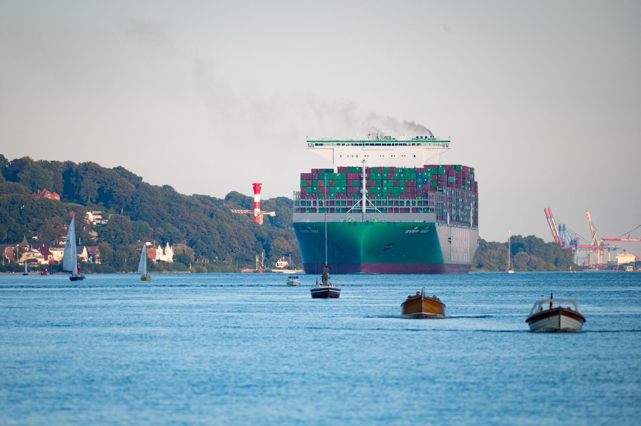 Ein Containerschiff fährt mit anderen Kleinbooten und Segelschiffen auf der Elbe vor Blankenese.