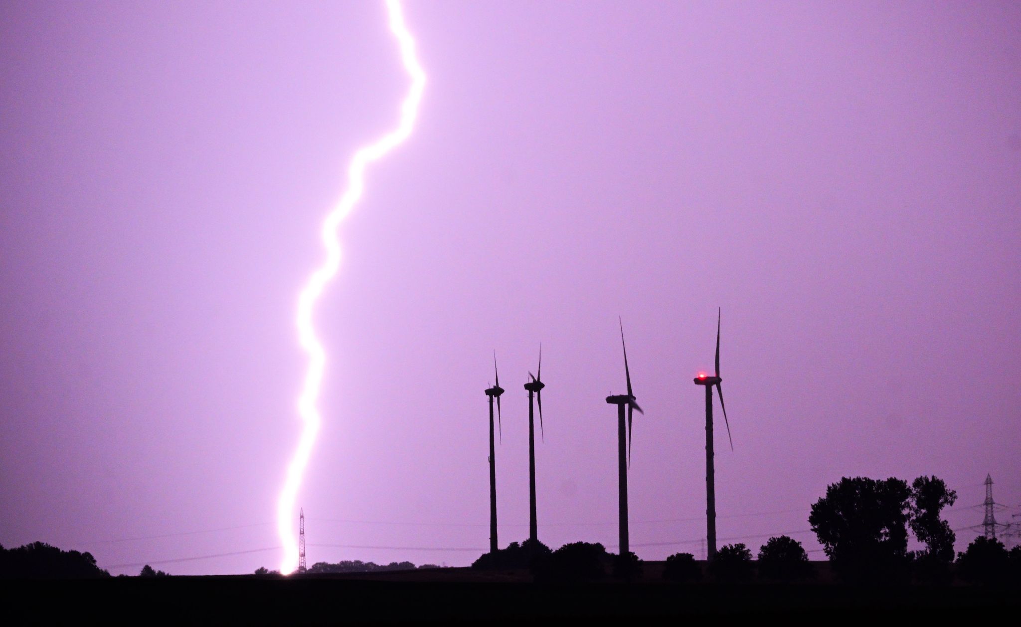 Ein Blitz entlädt sich während eines Gewitters hinter Windrädern.